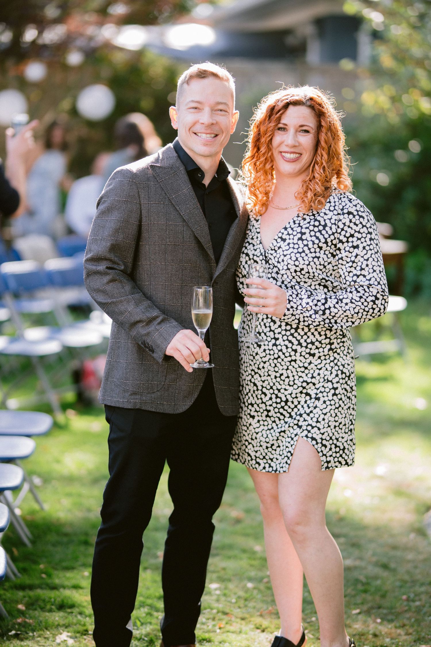 Couple in polka dot dress and dark suit enjoying drinks at an outdoor party.