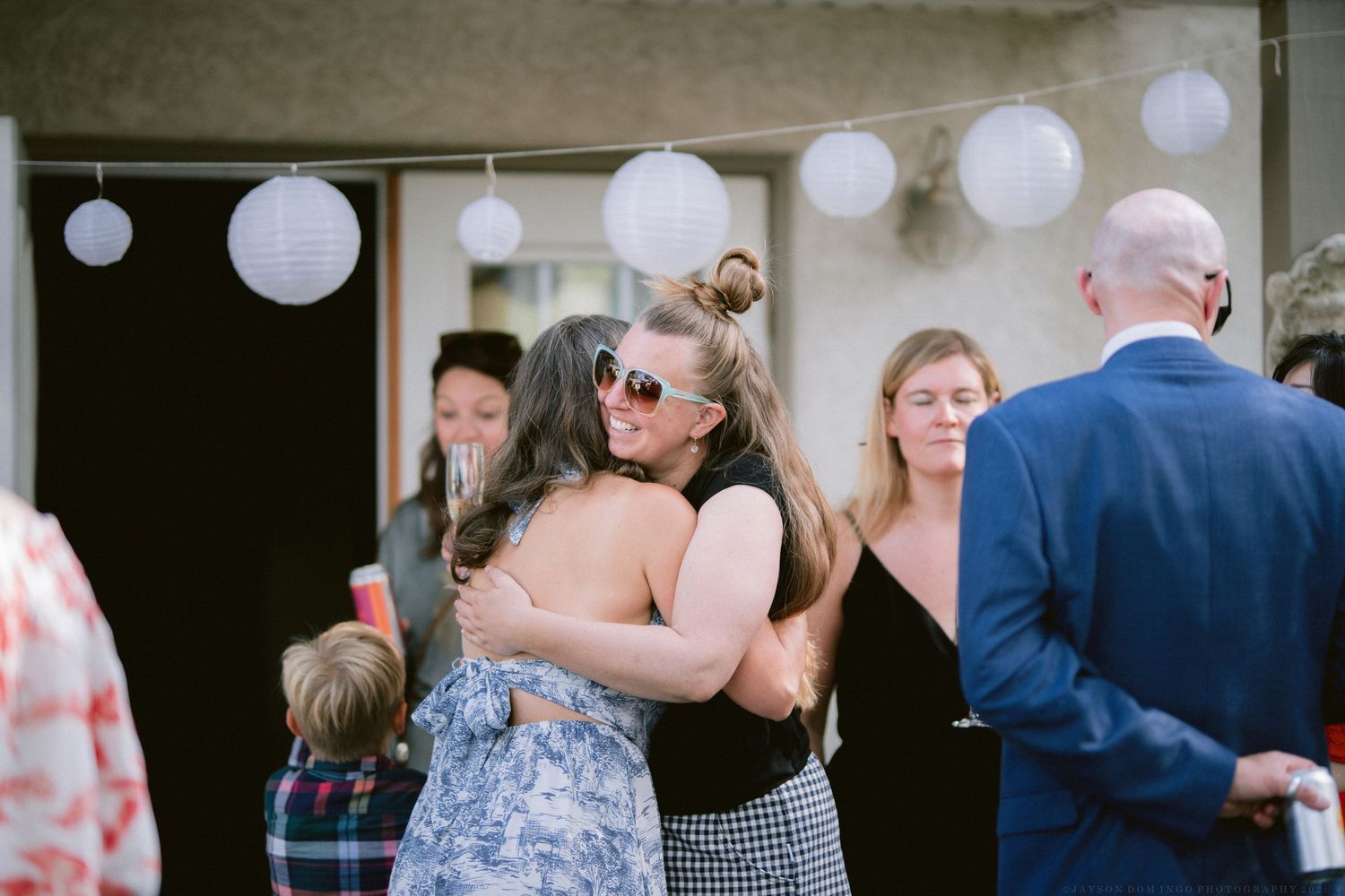 Wedding guests dance and socialize under white paper lanterns at an outdoor reception venue.