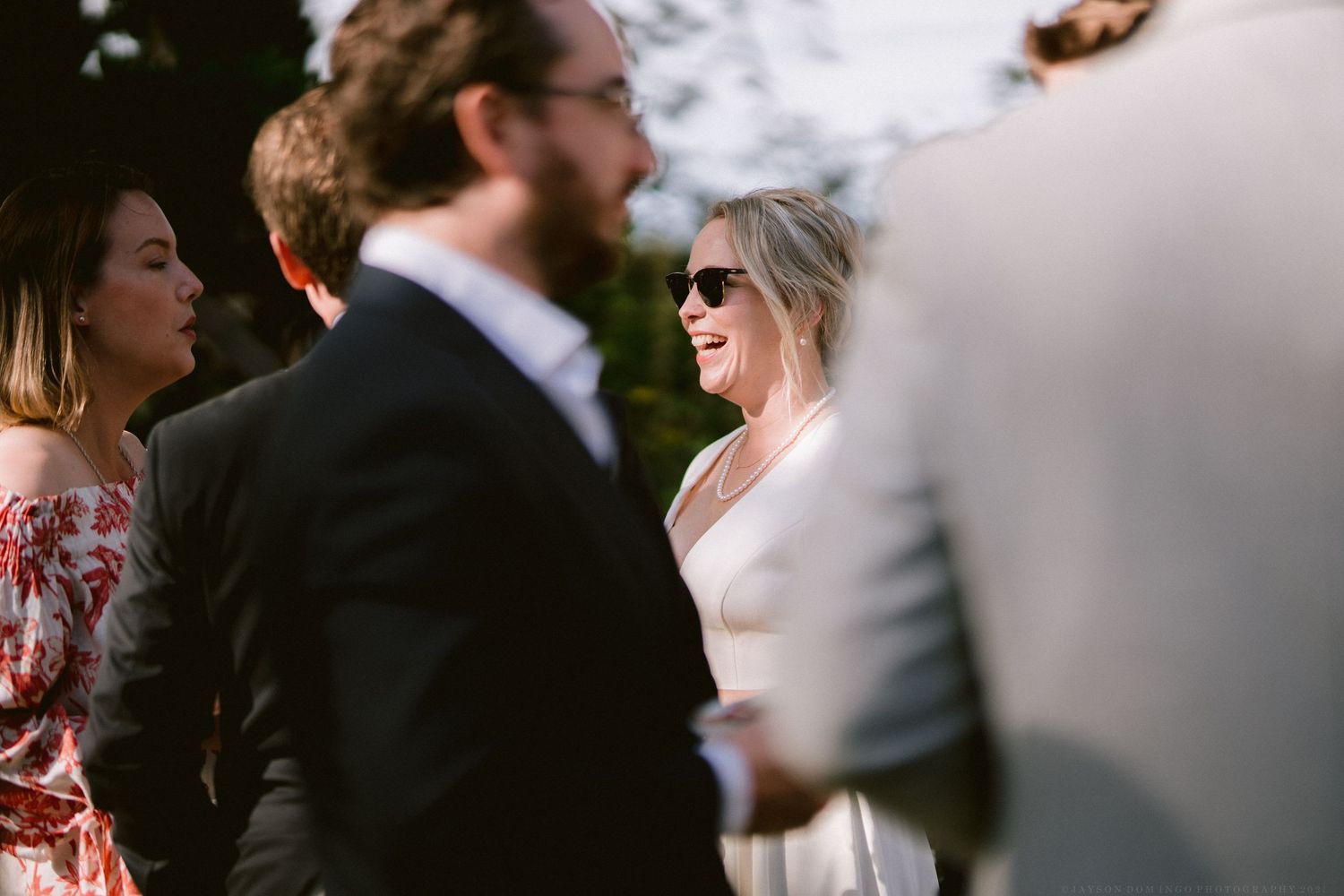 Wedding guests in formal attire gathered outdoors during a ceremony.