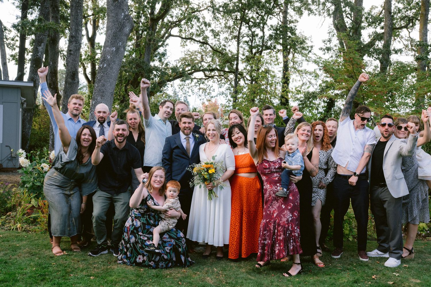 Wedding party and guests pose together for outdoor group photos in a garden setting.