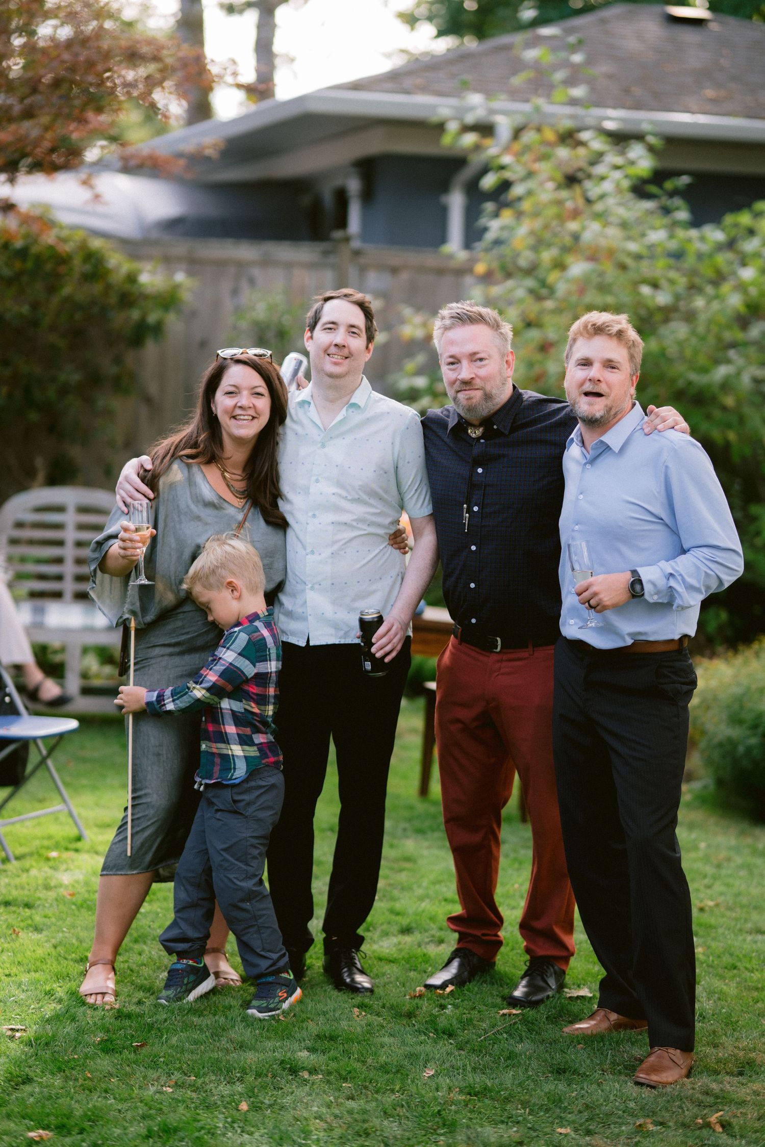A group of people standing together and laughing in a backyard garden setting.