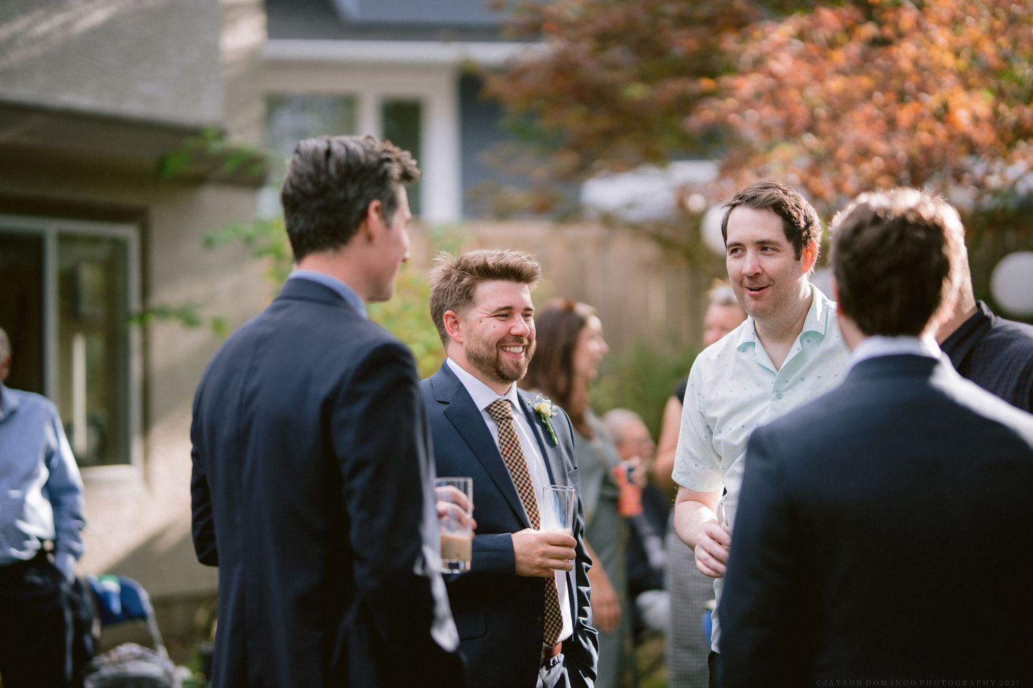 Wedding guests gathered outdoors in autumn enjoying drinks and conversation during a reception.