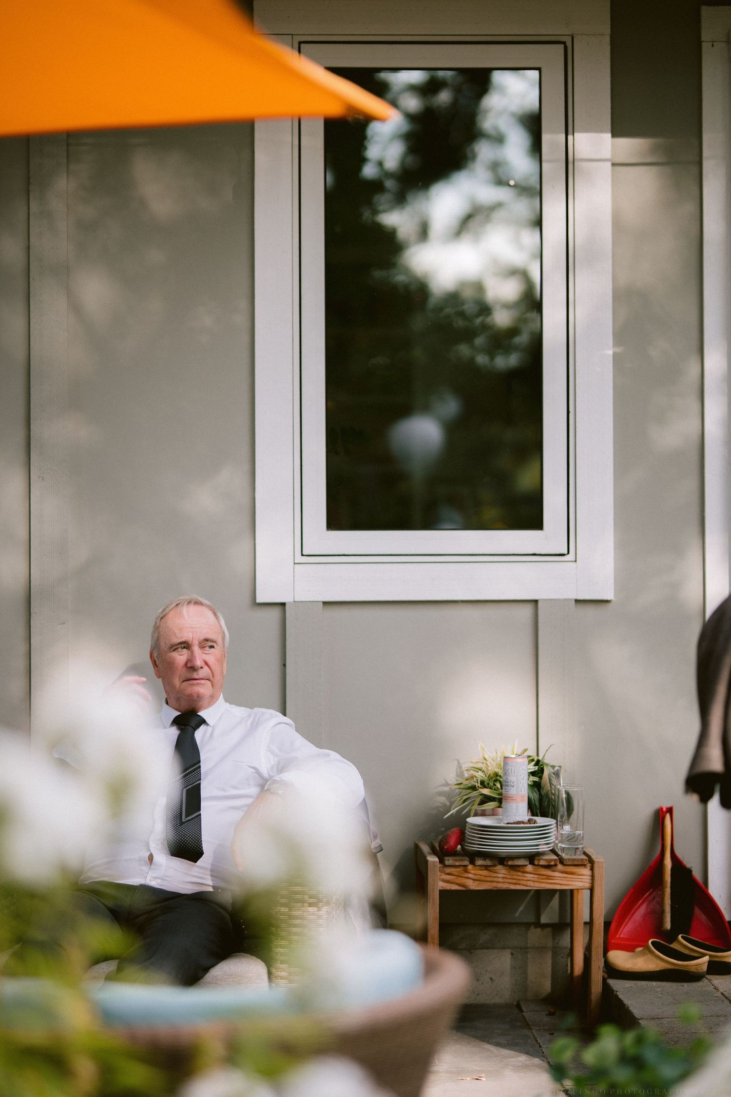 People gathered on a covered porch with white walls and blurred foliage in the foreground.