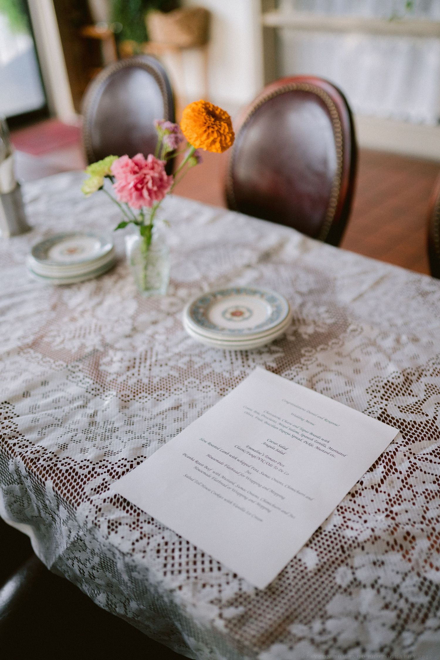 Wedding menu cards and place settings displayed on an elegant white lace tablecloth with delicate floral accents.