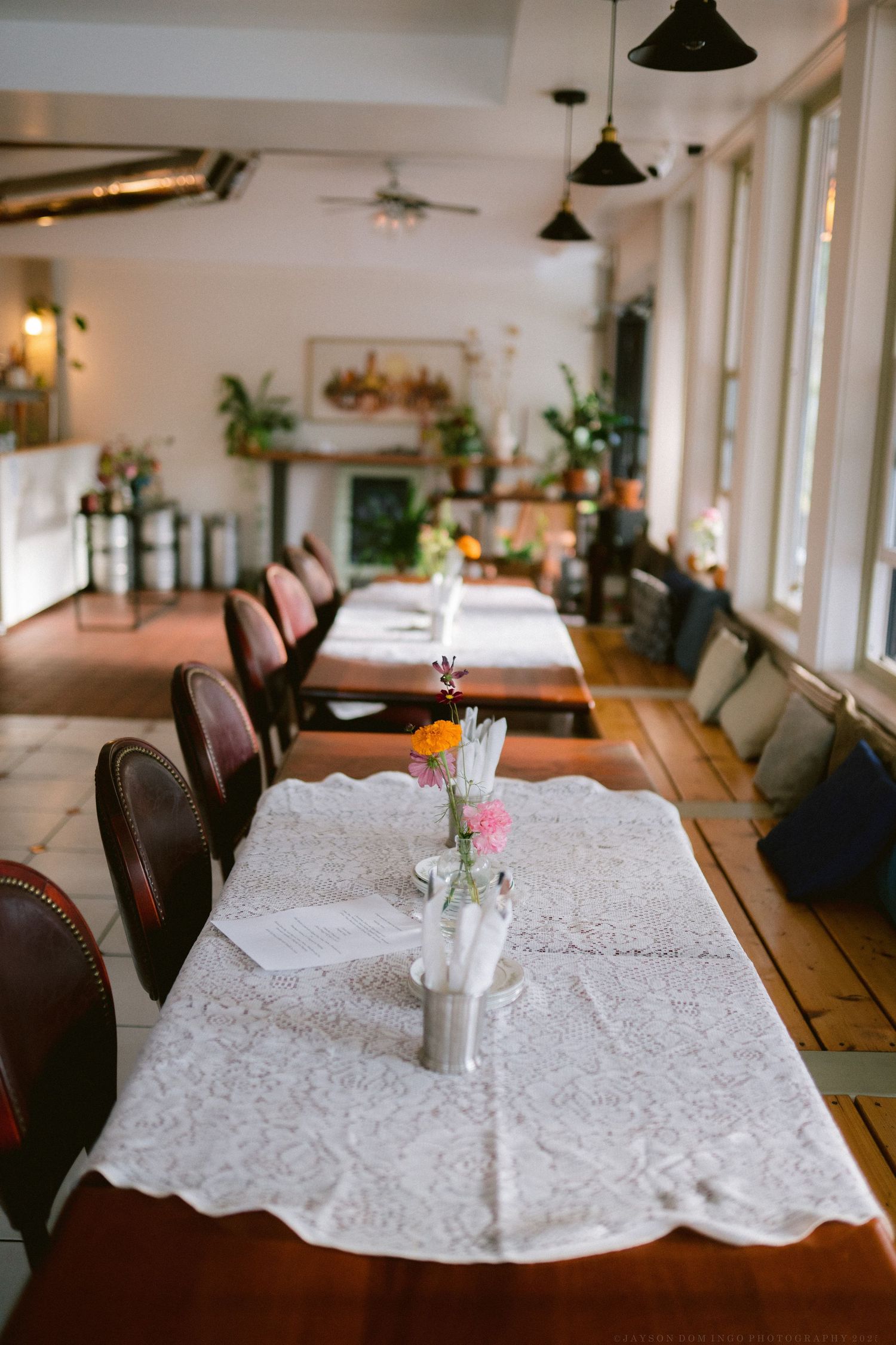 Elegant restaurant interior with white lace tablecloths and dark wooden chairs in natural lighting.
