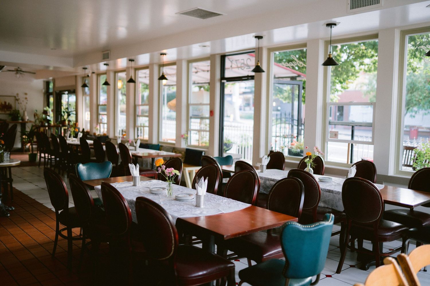 Interior view of a modern cafeteria with large windows, wooden tables and blue chairs in natural lighting.