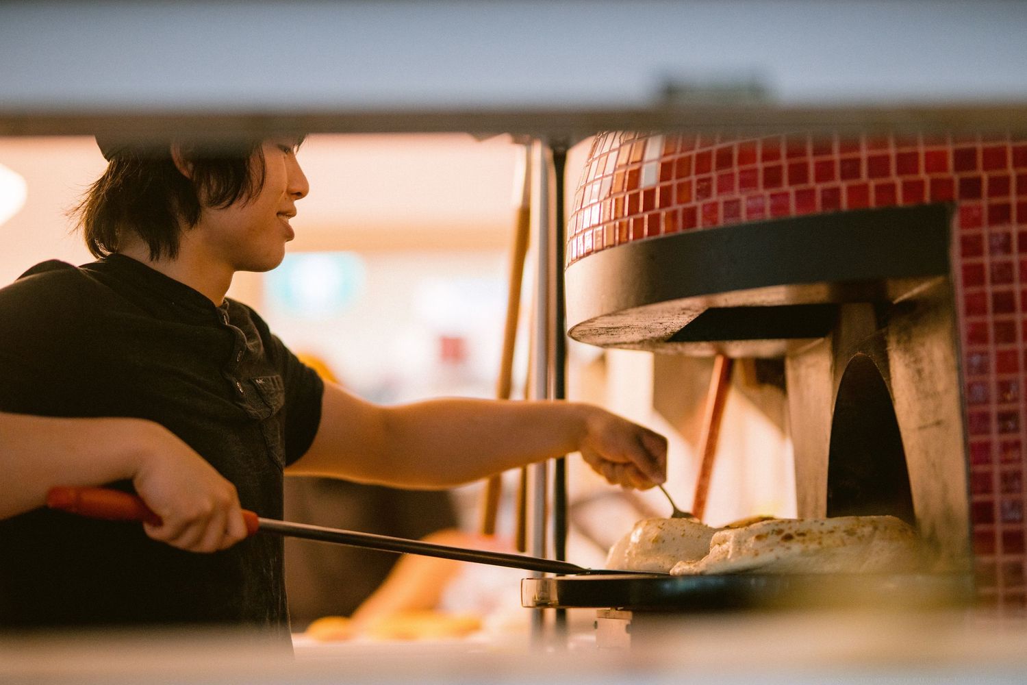 Chef placing pizza into a traditional brick pizza oven with red tile interior and glowing flames.