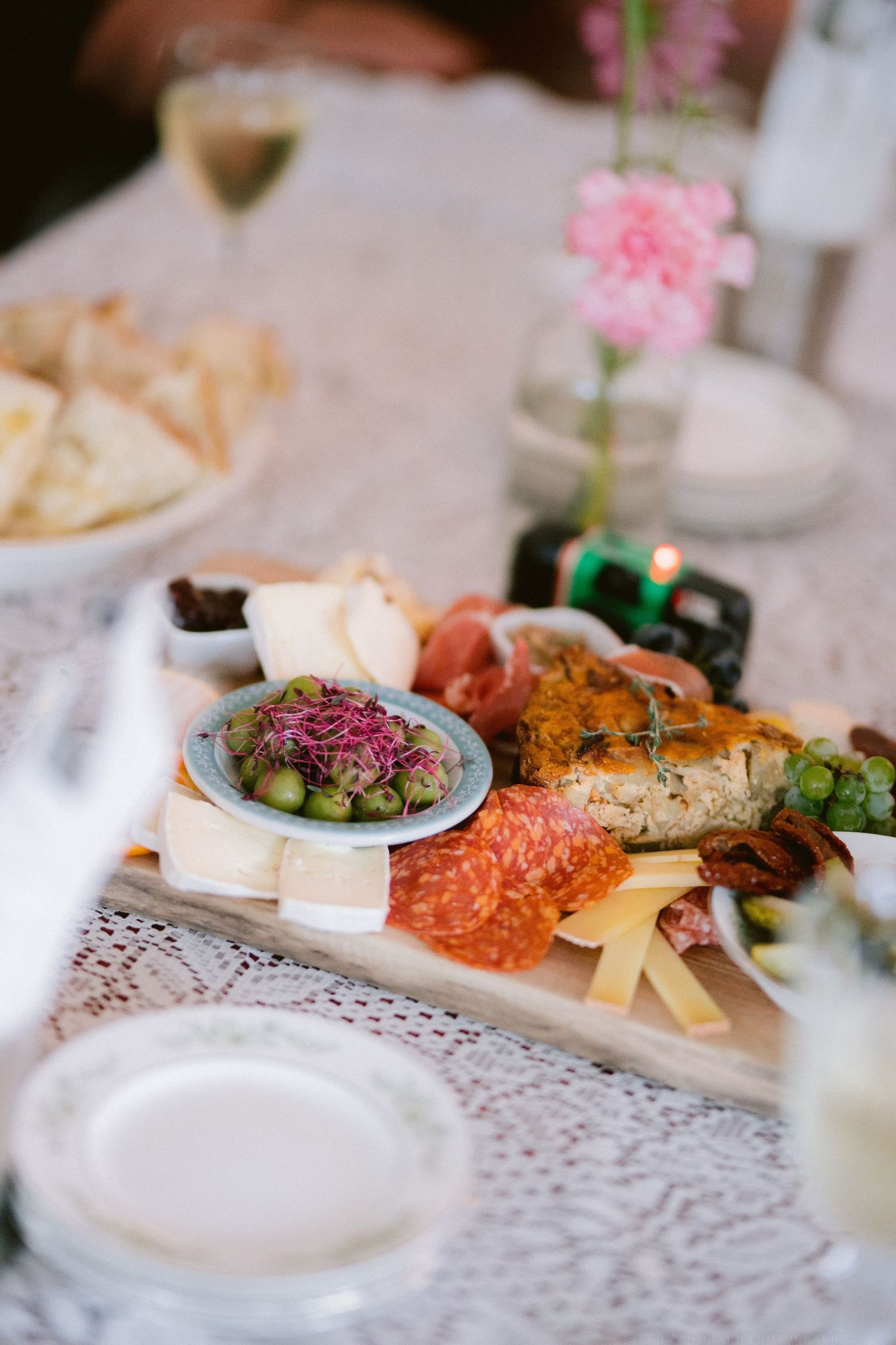 An elegant wedding reception table setting with charcuterie boards featuring meats, cheeses and garnishes on lace tablecloths.