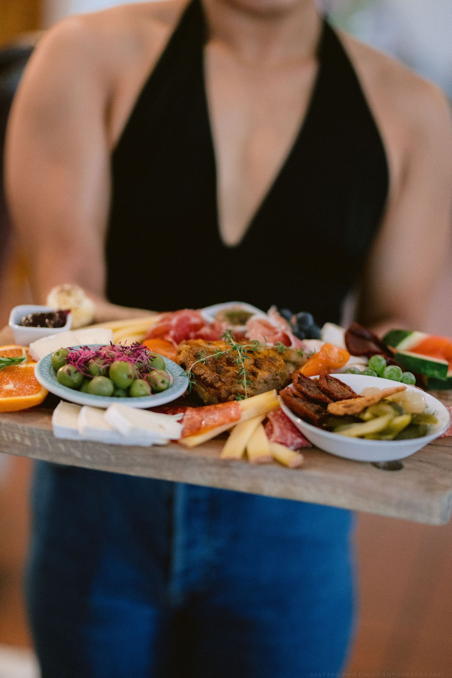A wooden charcuterie board displays an assortment of meats, cheeses, fruits and olives for entertaining.