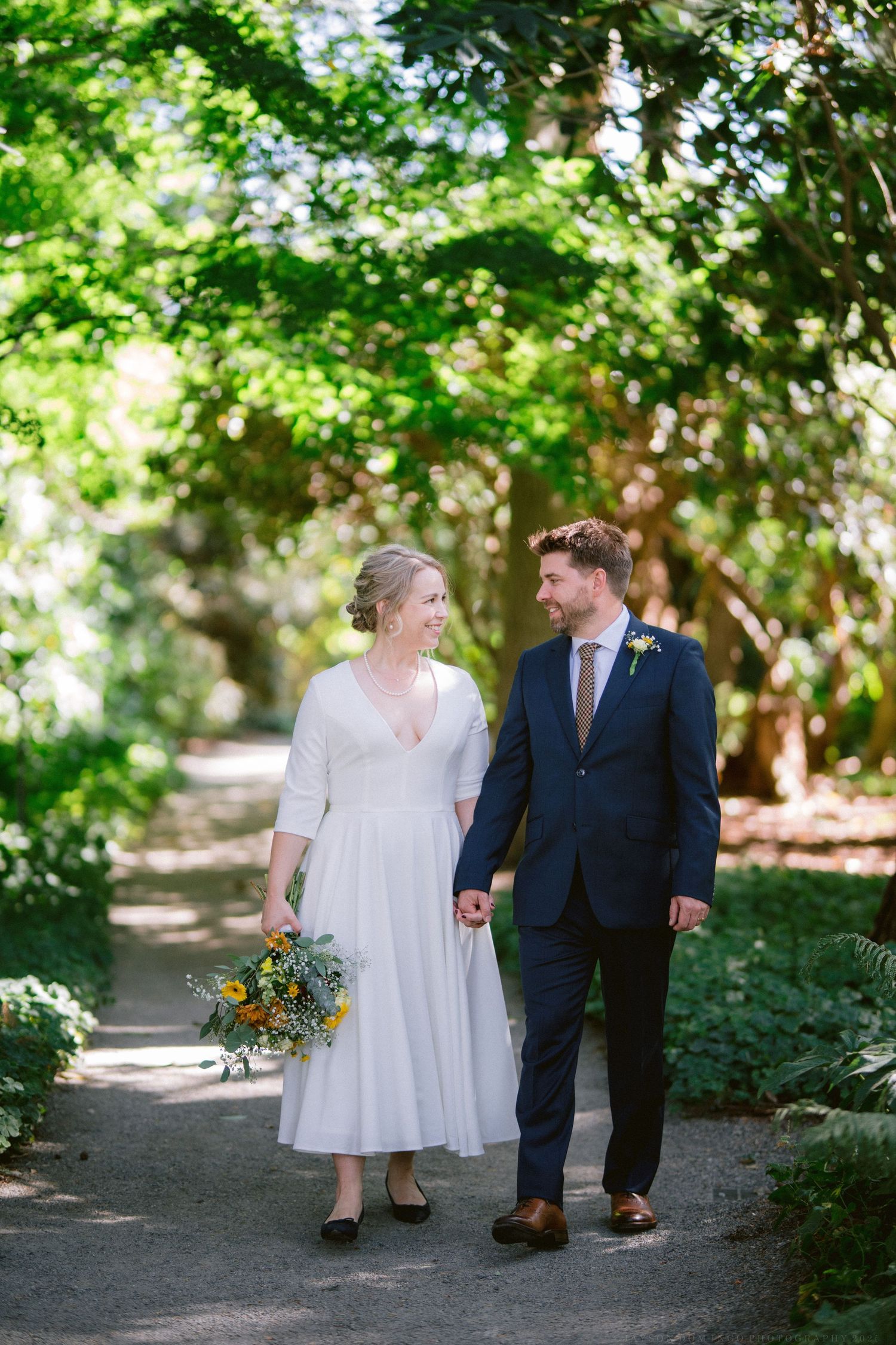 Couple walking together on garden path surrounded by lush greenery.
