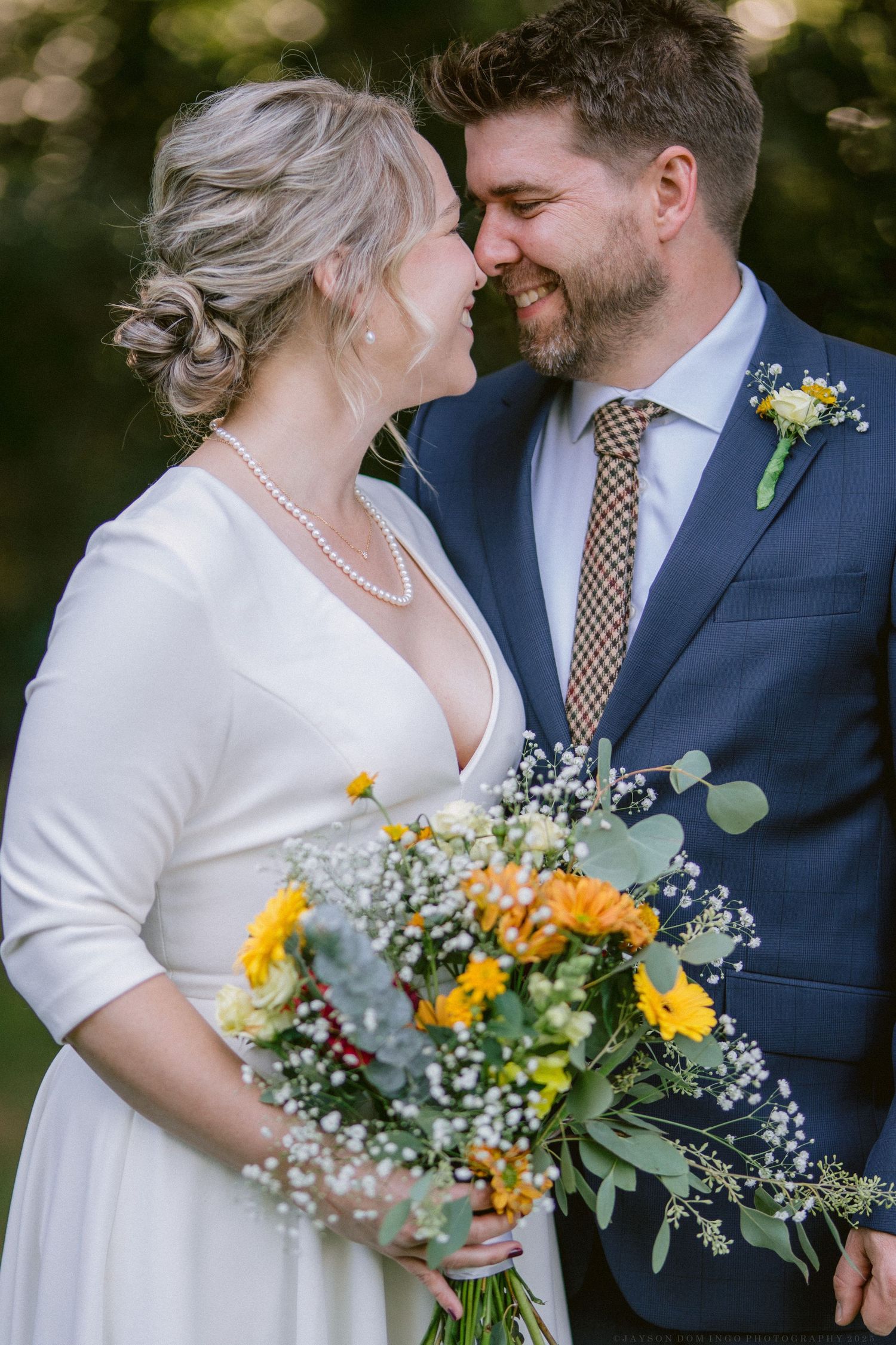 Newlyweds share intimate moments while holding a bouquet with yellow flowers and baby's breath.