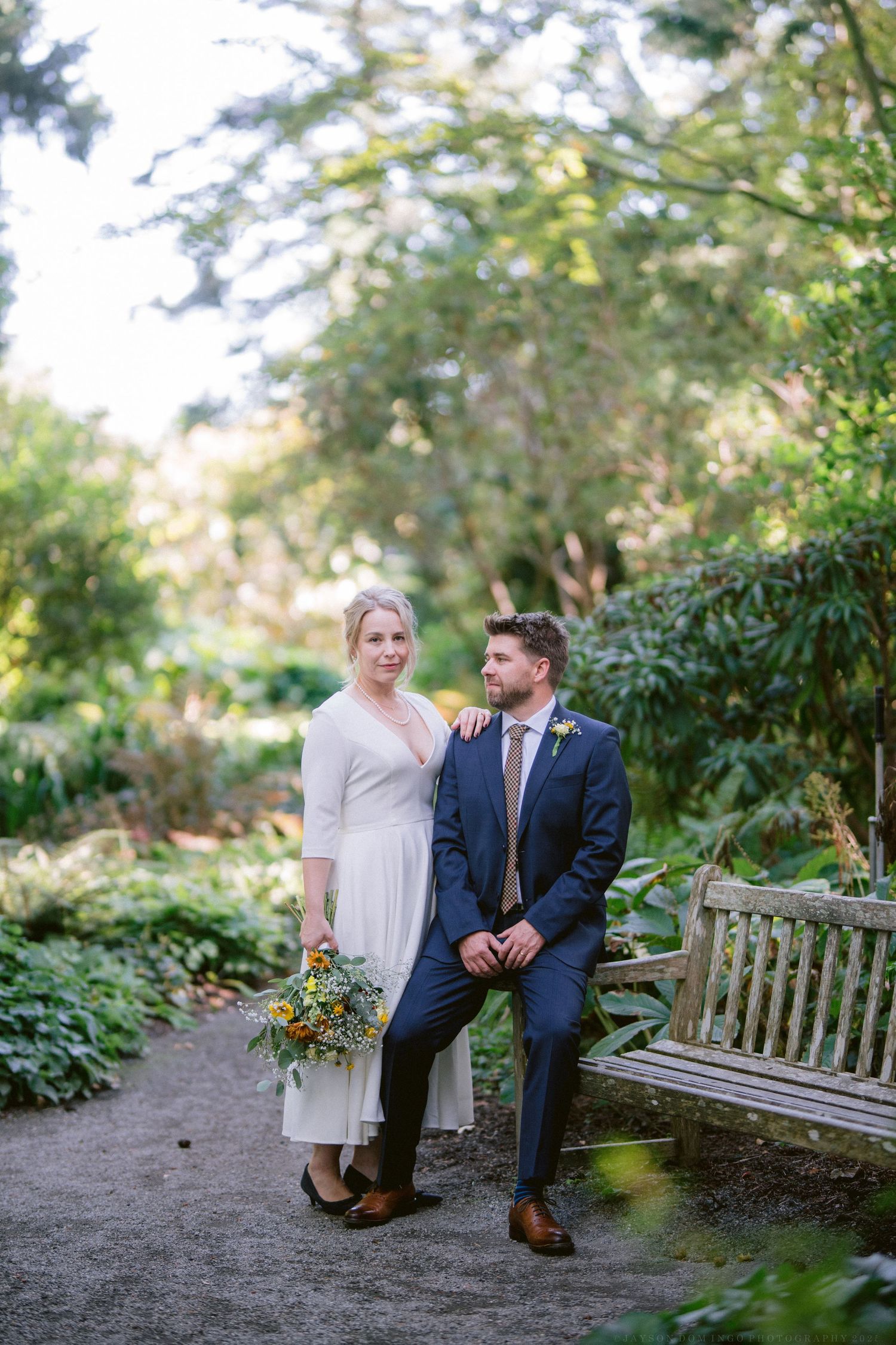 Couple sitting on wooden garden bench surrounded by lush greenery.