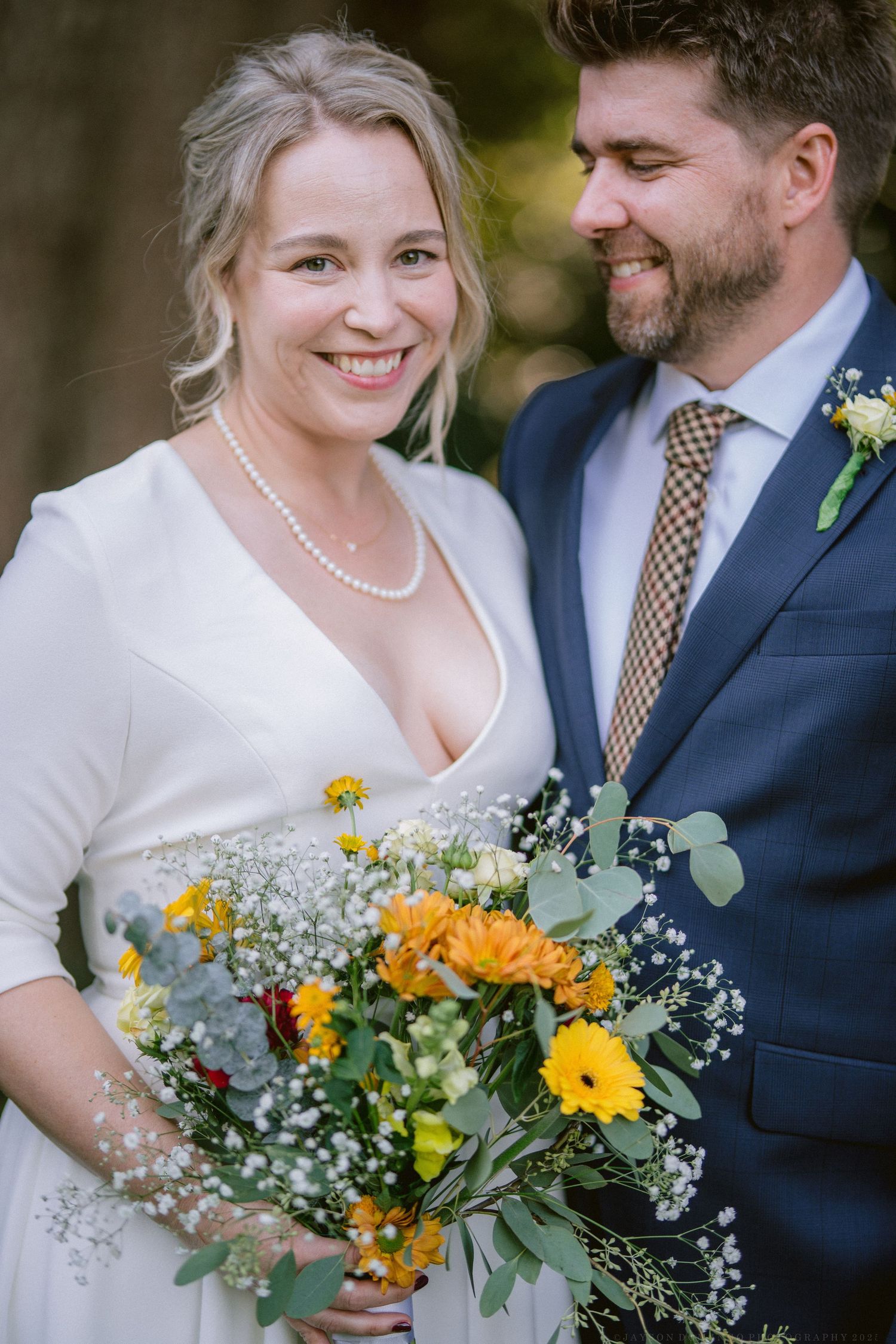 Wedding couple with vibrant yellow and orange bouquet featuring sunflowers and greenery.