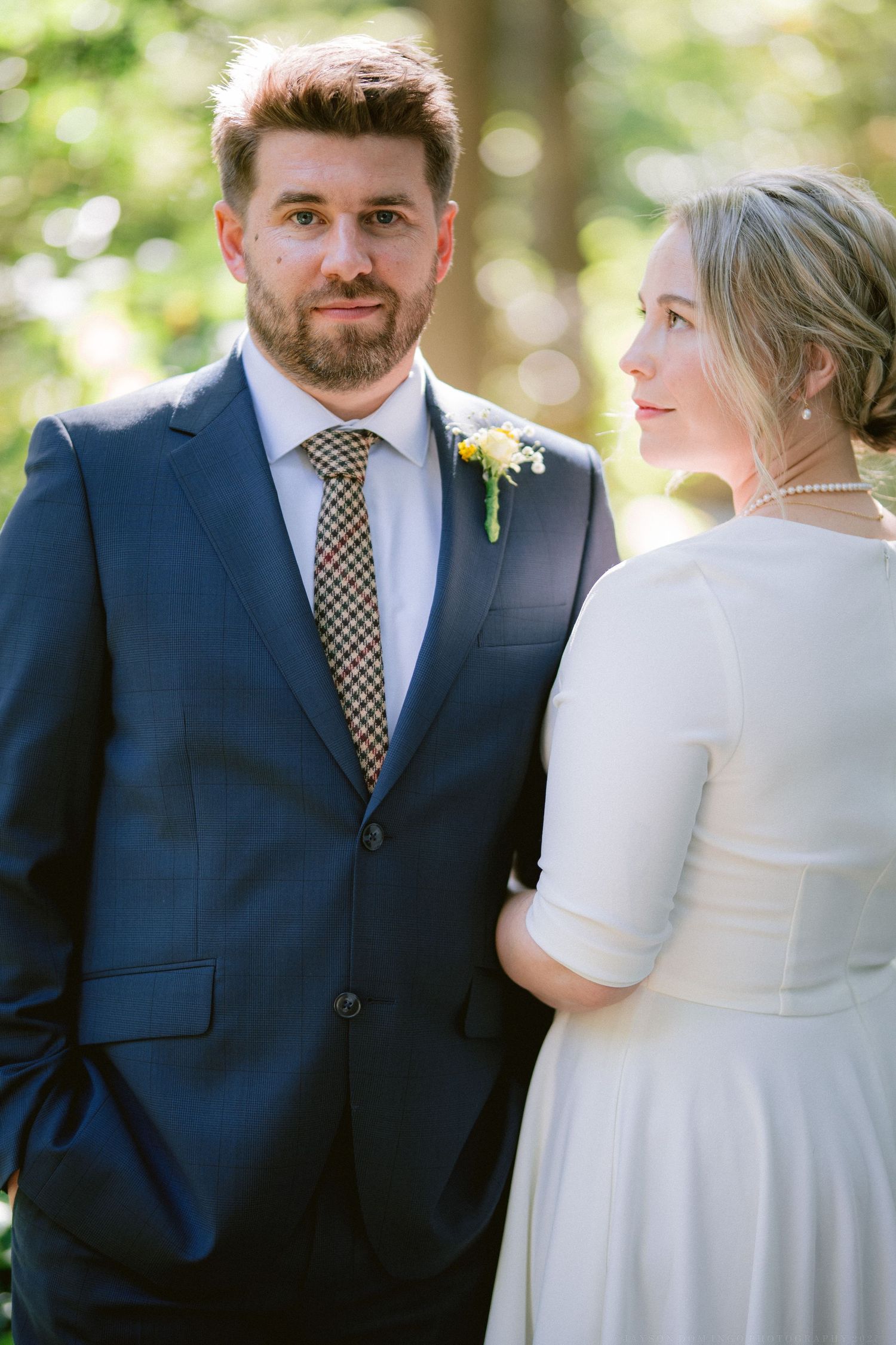 Wedding couple in white dress and navy suit sharing intimate moment outdoors.