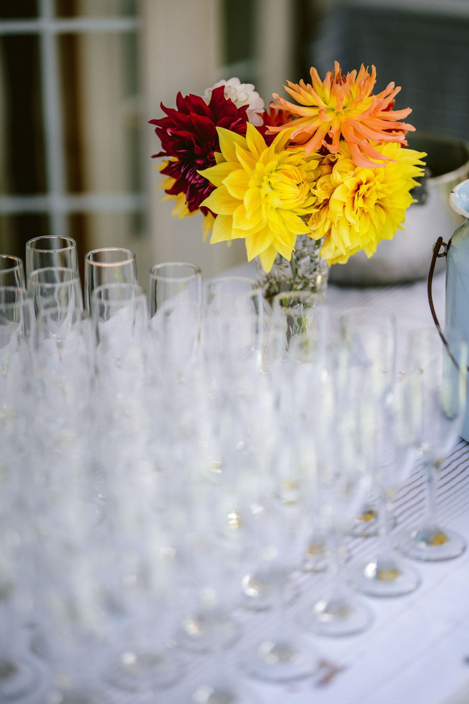 Reception table setting with bright yellow and orange dahlias in glass vases.
