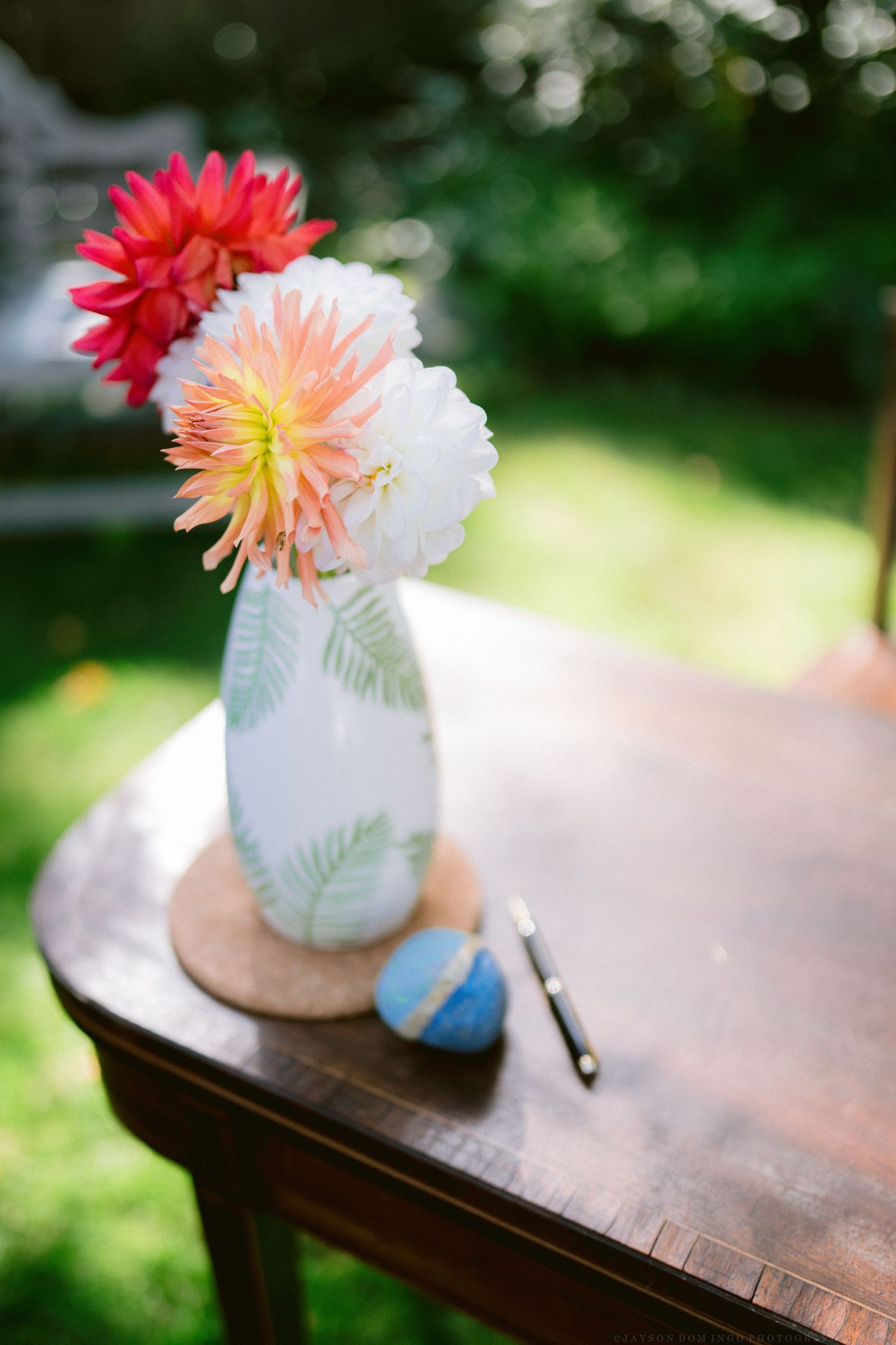 Colorful dahlia flowers in painted vases arranged on wooden surface with soft bokeh background.