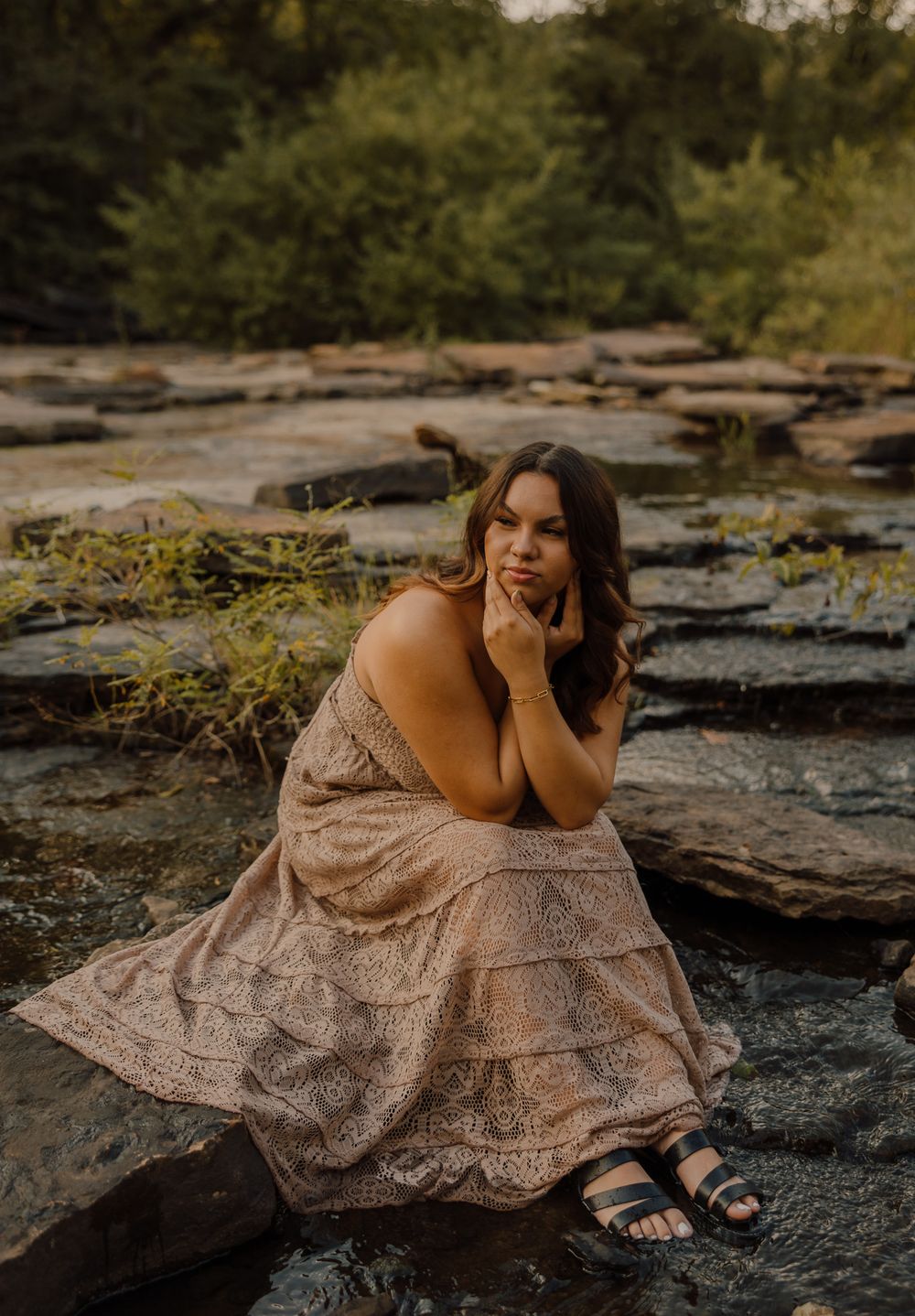 A person in a beige lace dress poses gracefully on dark rocky terrain during a moody outdoor photoshoot.