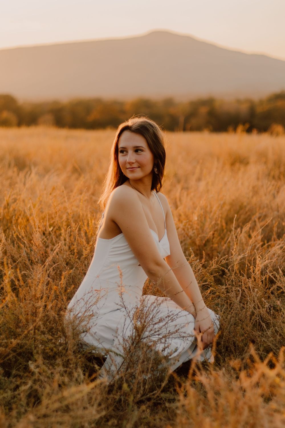 A figure in a white dress sits gracefully in a golden wheat field at sunset, creating a dreamy summer portrait.