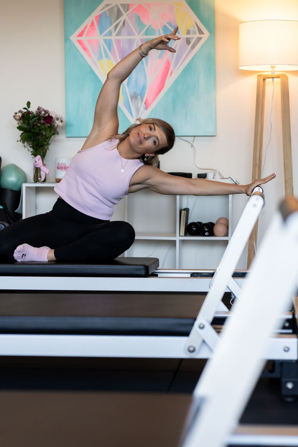 Person stretching on a reformer pilates machine with colorful geometric artwork in the background.