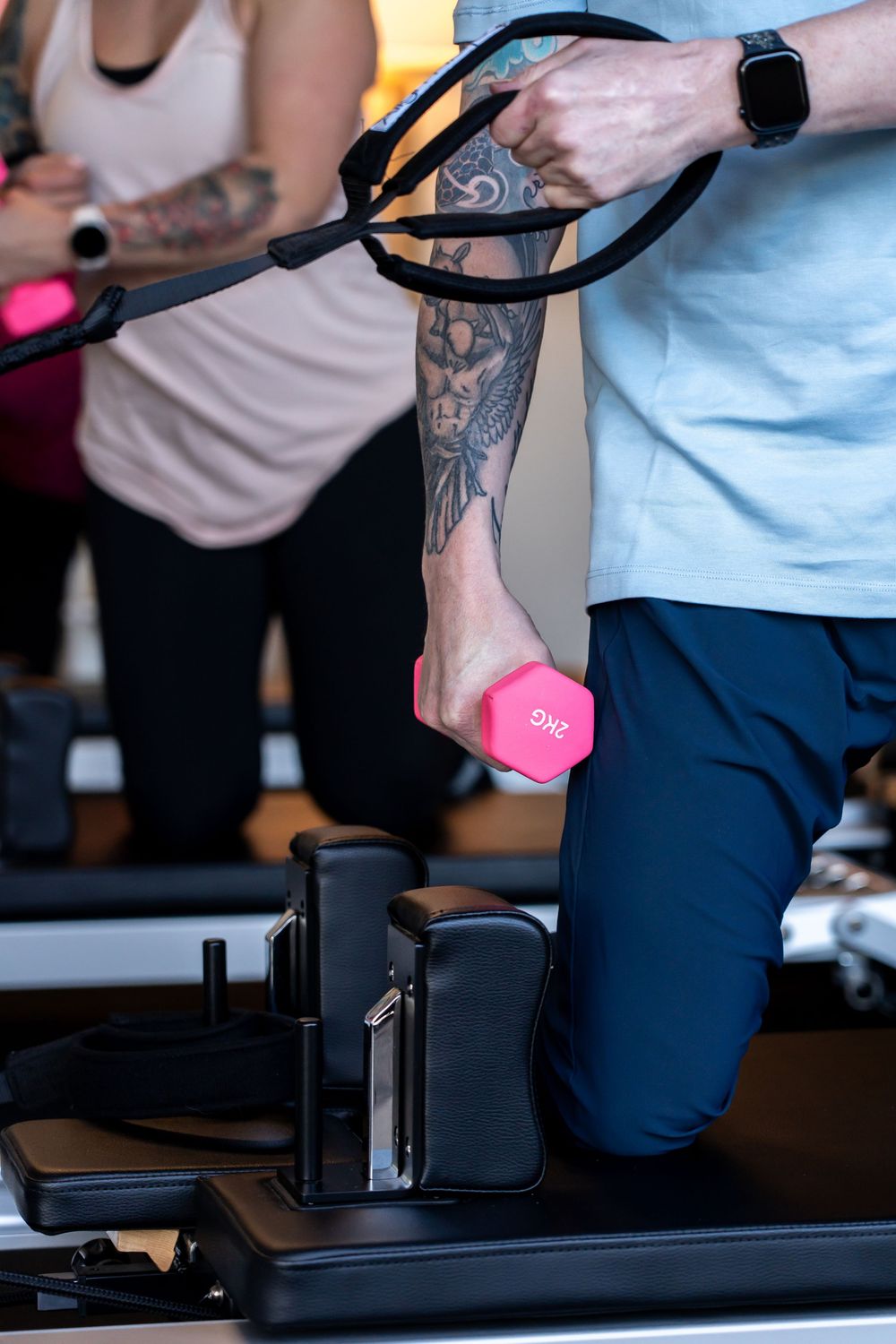 Close-up of tattooed arms holding pink dumbbells during workout session.