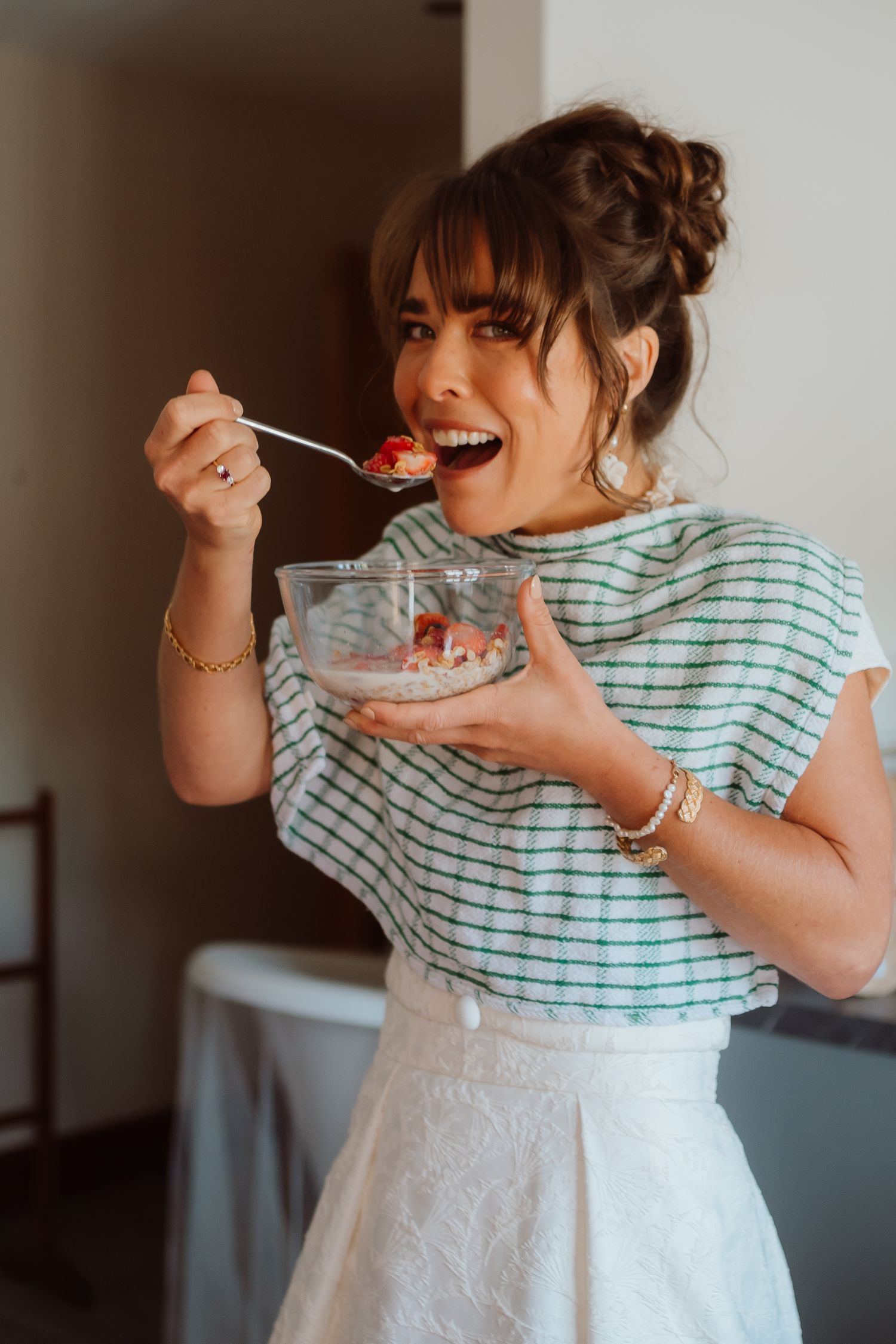 A person in a striped shirt and white dress enjoys eating strawberries in a sequence of candid photos.