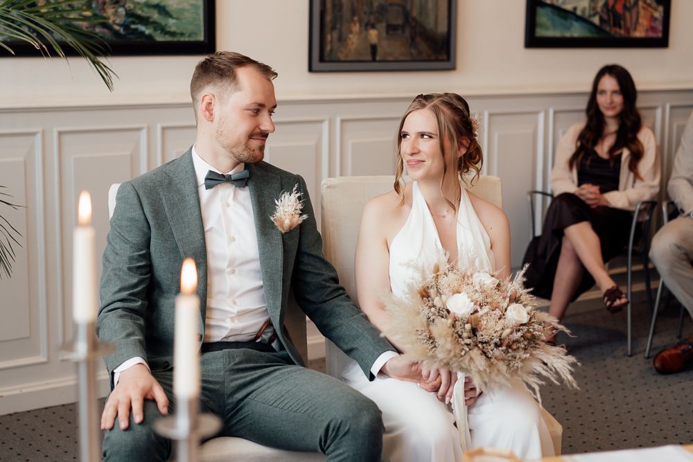 A couple sits together at their intimate wedding ceremony with dried floral bouquet and elegant attire.
