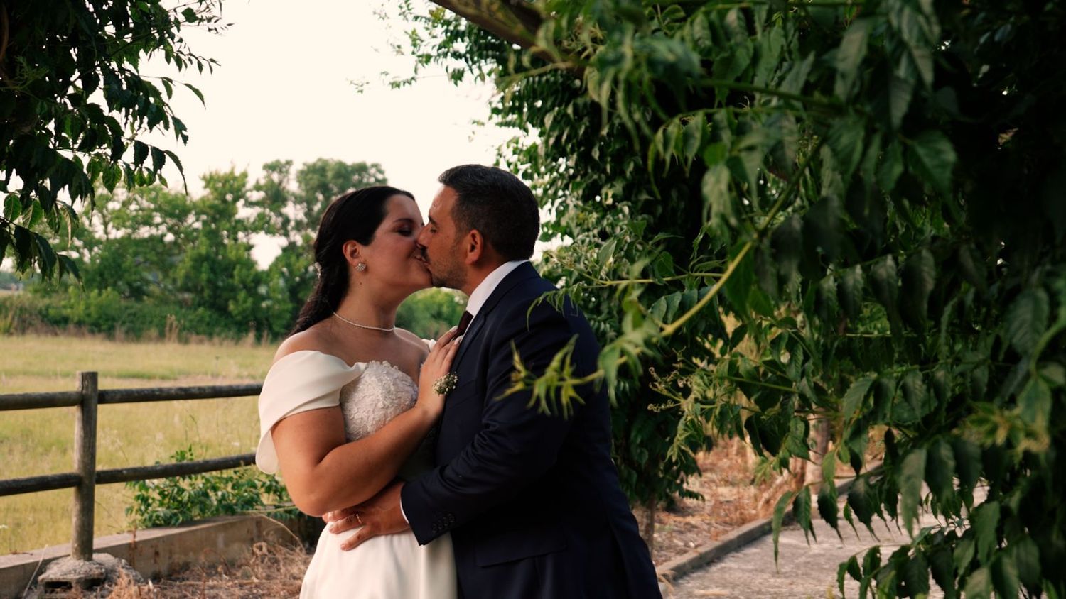 A romantic engagement photoshoot under leafy green trees in a rustic outdoor setting.