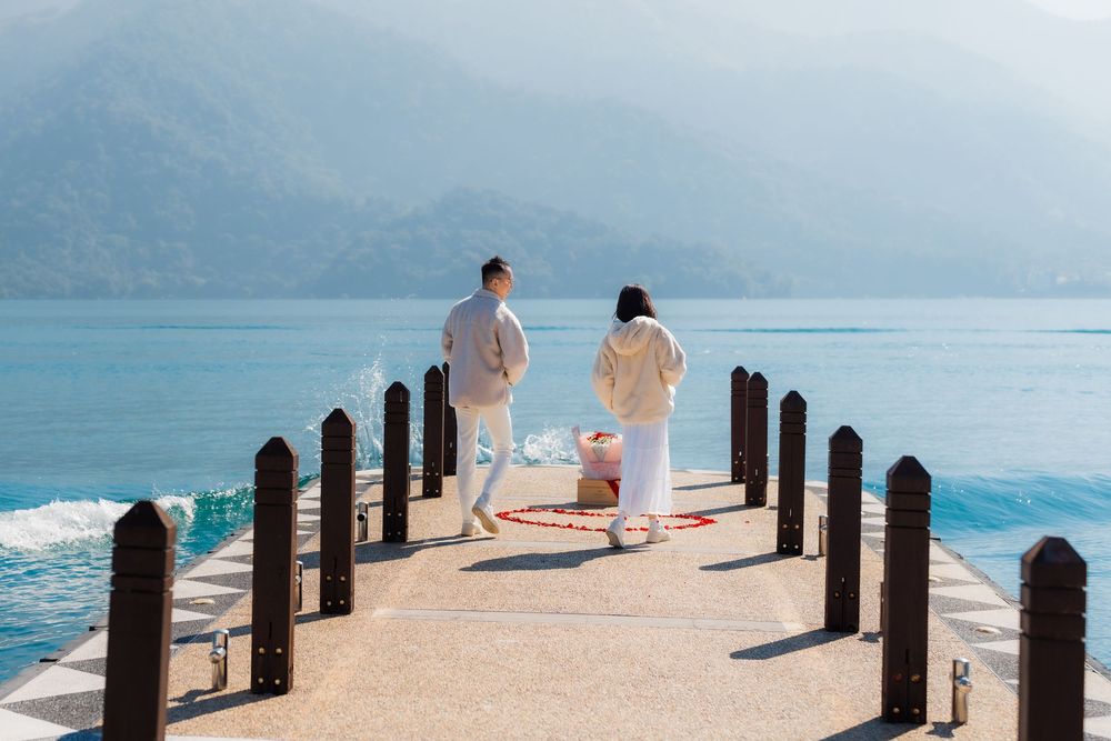 A couple in coordinating white outfits walk along on a serene mountain lake on a misty morning.