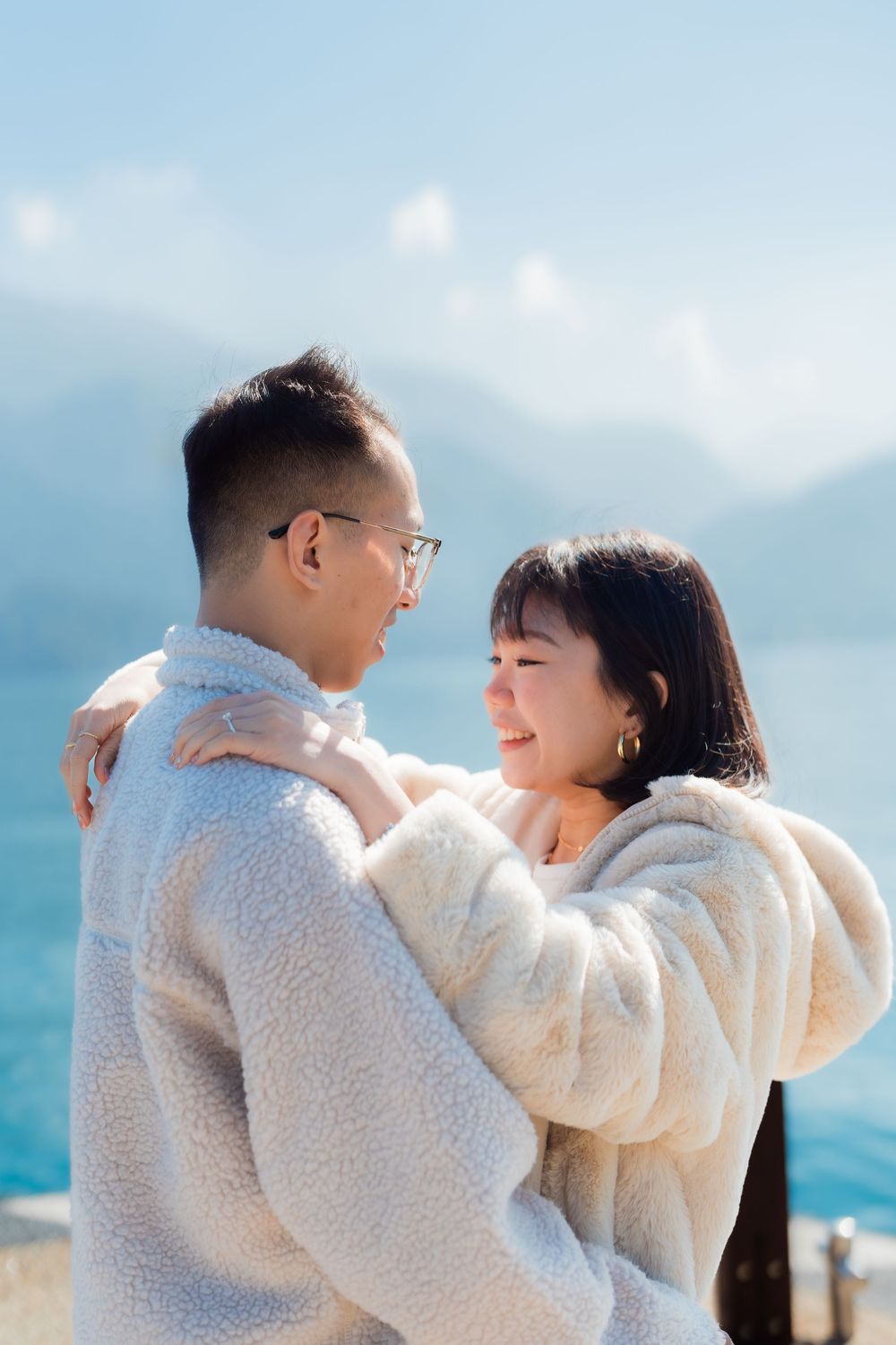 A couple in matching white sweaters share an intimate moment against a scenic misty mountain backdrop at Sun Moon Lake, Taiwan,