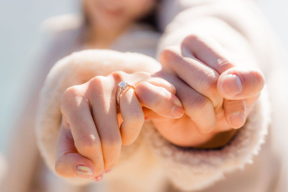 Close-up view of hands holding each other tenderly, showing of an engagement ring with sunlight creating a soft, warm glow.