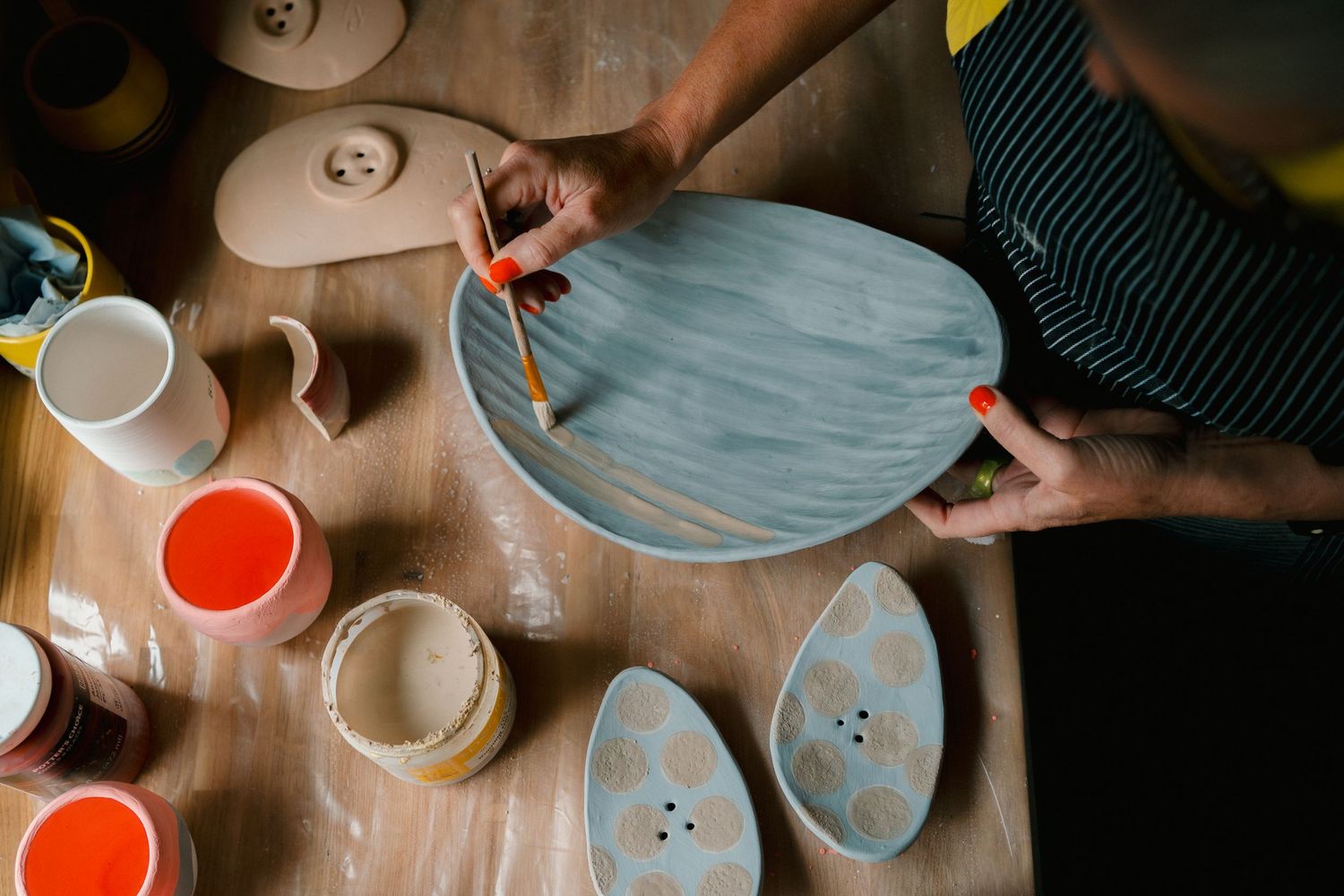 Hands carefully decorating a cake with colorful frosting and sprinkles on a wooden surface.