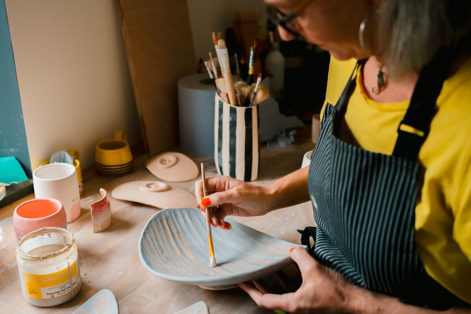 Person in striped apron and yellow shirt piping frosting onto a cake during decorating process.