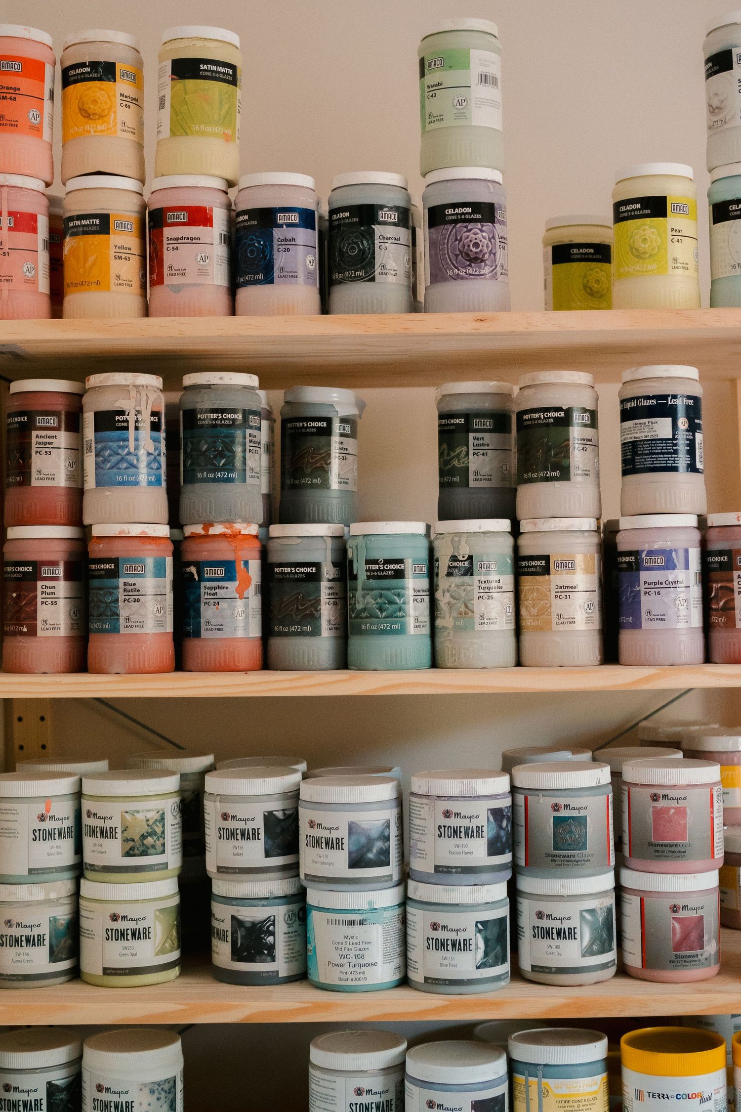 Rows of paint jars neatly arranged on wooden shelves showcase various colors and sizes of art supplies in a studio setting.