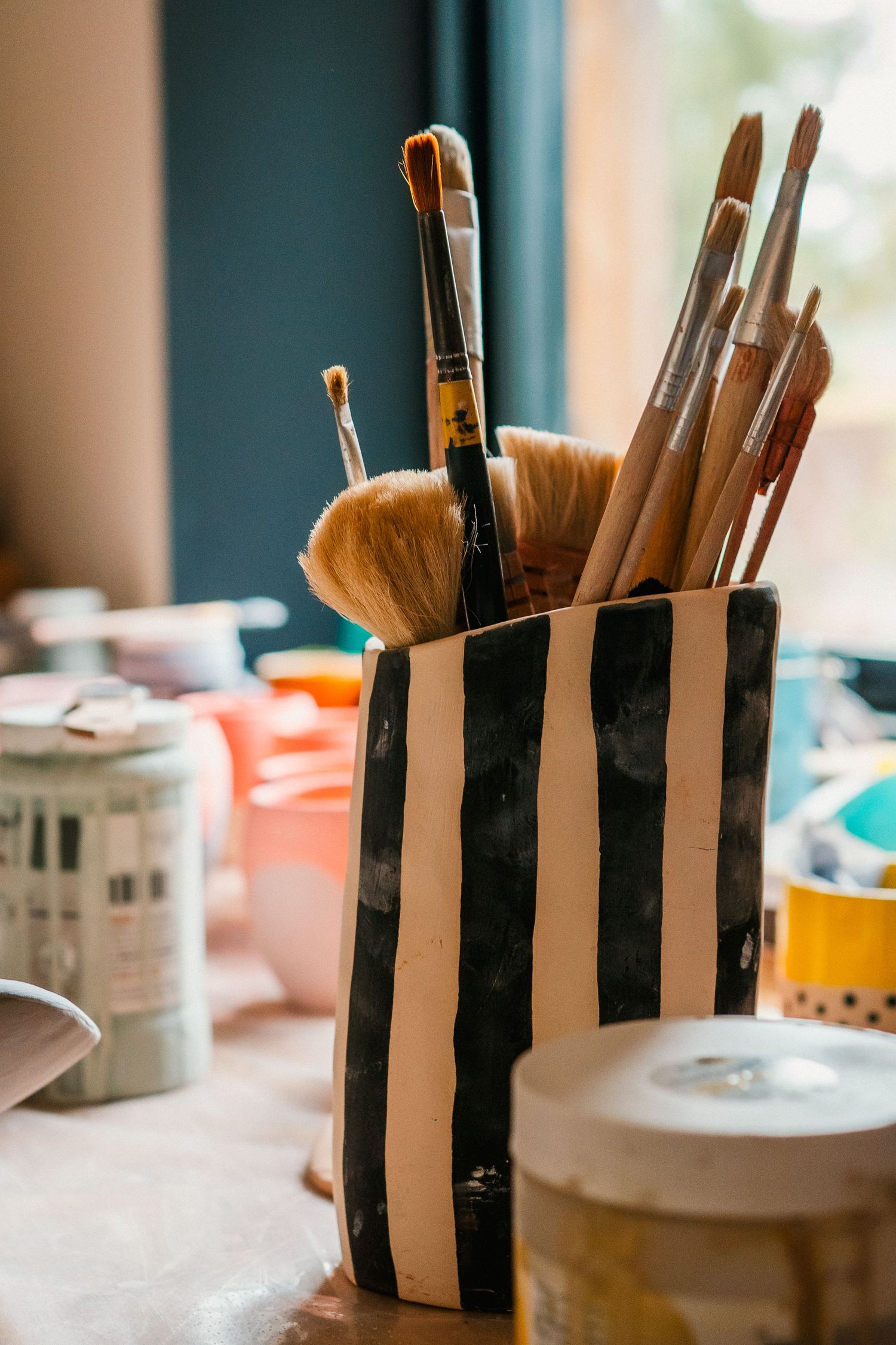 A sequence of artistic paintbrushes arranged in a striped black and white ceramic holder on a light surface.