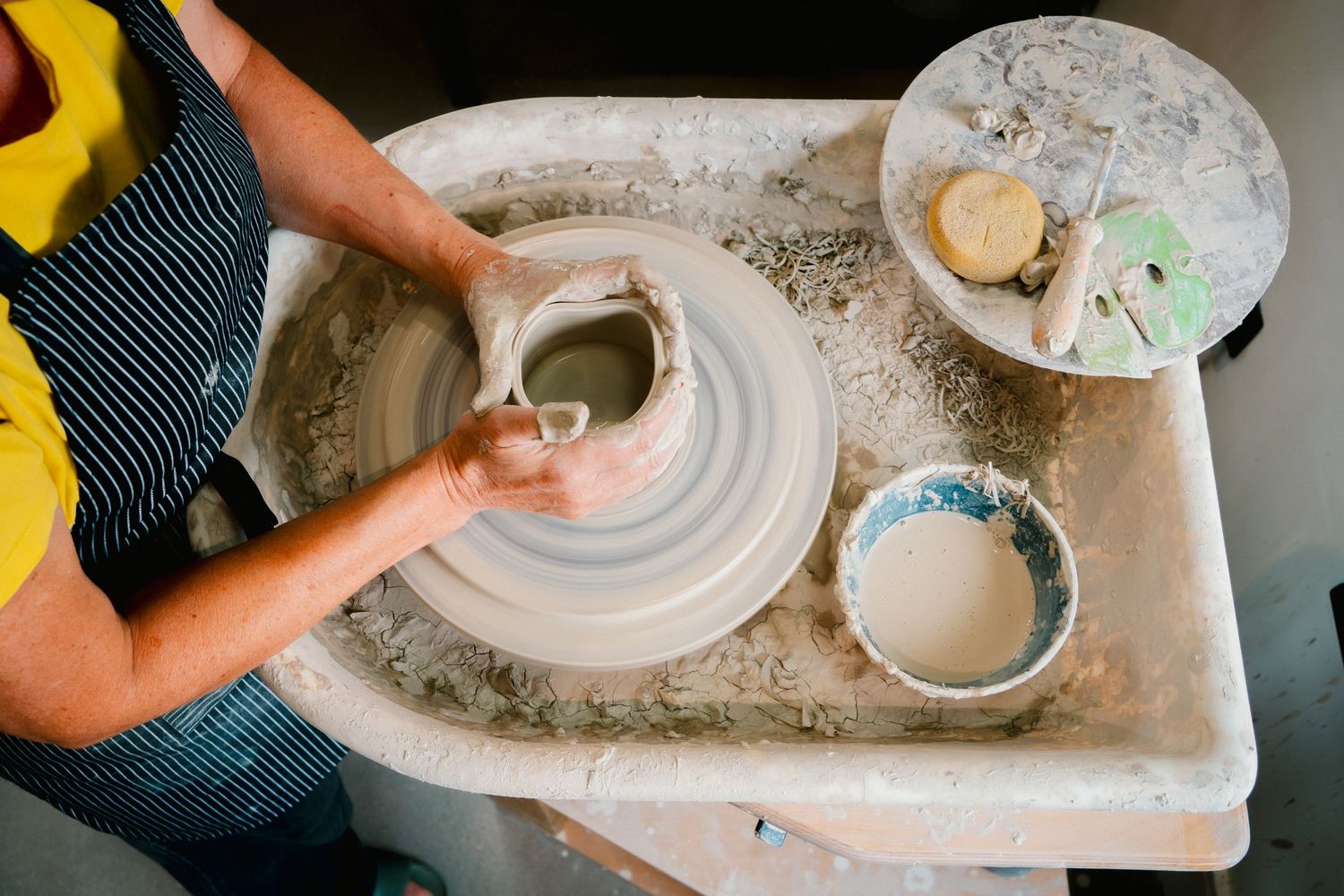 Close-up view of hands working clay on a pottery wheel, shaping and forming a ceramic vessel with careful precision.