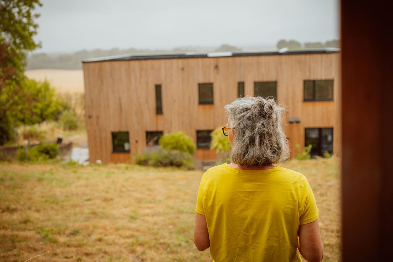 A person wearing a bright yellow shirt walks through a rustic outdoor setting with brick buildings in the background.