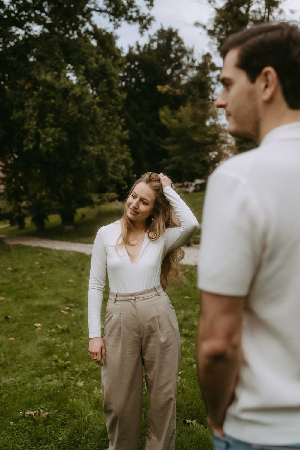 A couple in casual white and beige outfits share playful moments together in a grassy outdoor setting.