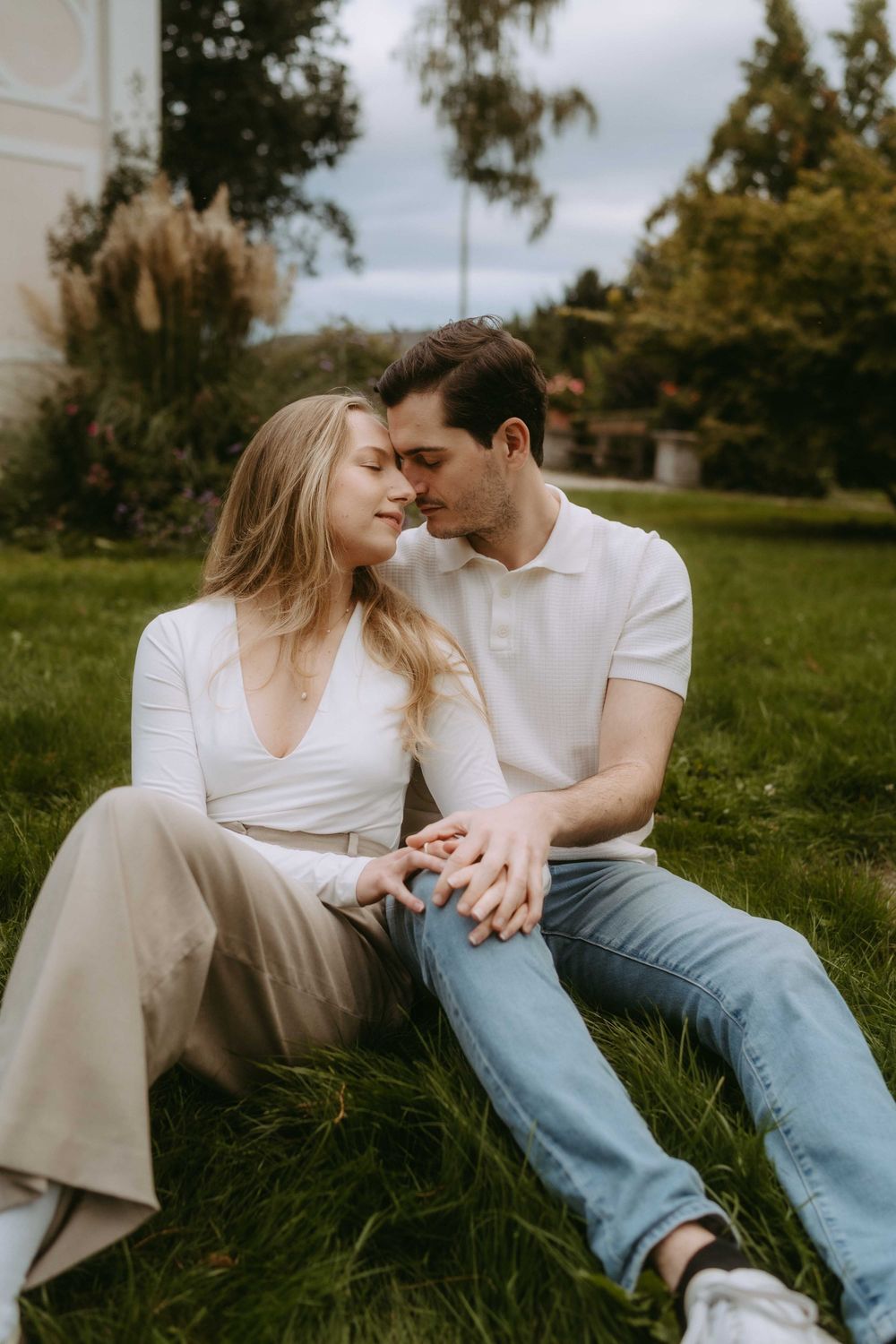 Two people in casual attire share intimate moments while sitting together on grass.