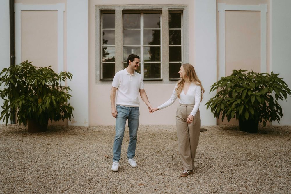 Casual couple walking along the exterior of a white building on a gravel path.