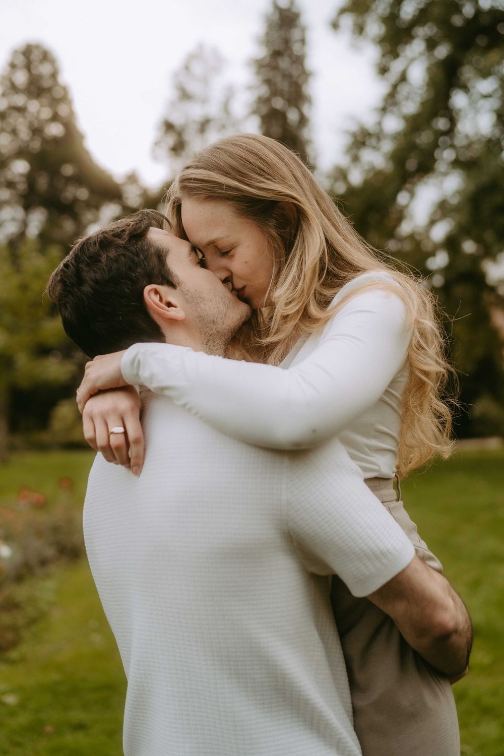 Romantic couple in white sweaters share tender embraces in an outdoor setting.