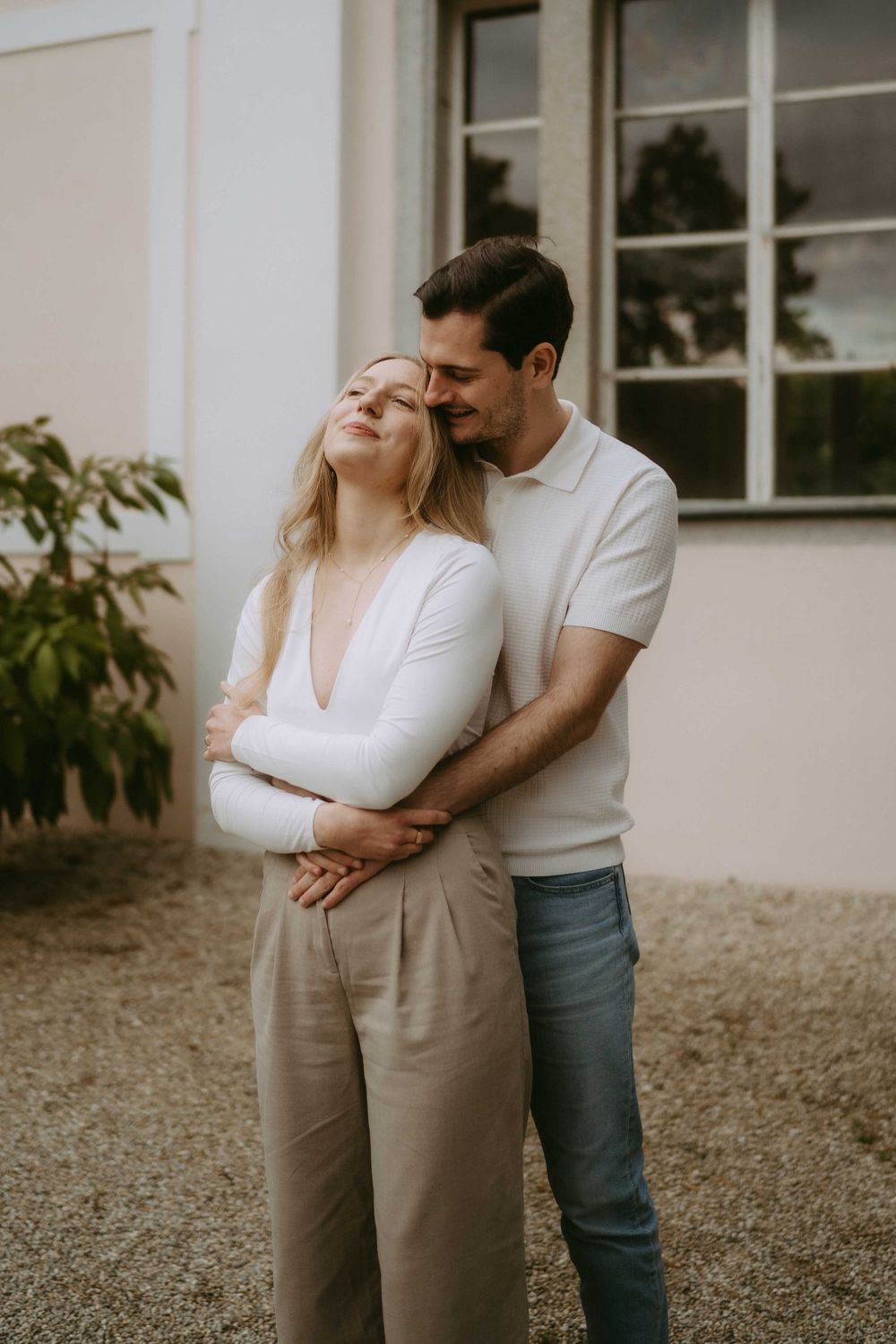 Intimate couple's portrait against white building exterior in casual attire.