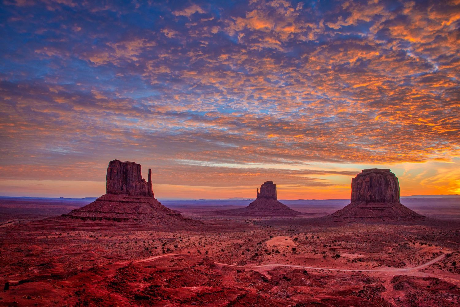 Panoramic sunset view of Monument Valley showing iconic red rock formations under dramatic orange and purple skies.