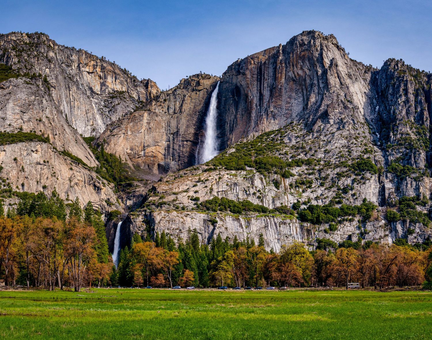 Panoramic view of Yosemite Valley showing granite cliffs, waterfalls, and autumn foliage under a clear blue sky.