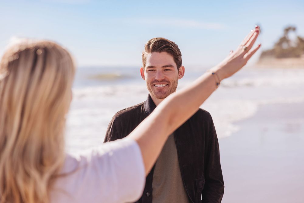 A couple shares a joyful moment together on a sunny beach with waves and sand in the background.