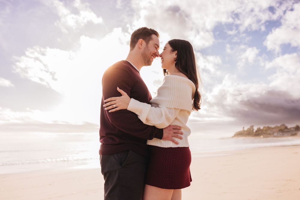 Romantic couple embraces on a beach at sunset with dramatic cloudy sky in the background.