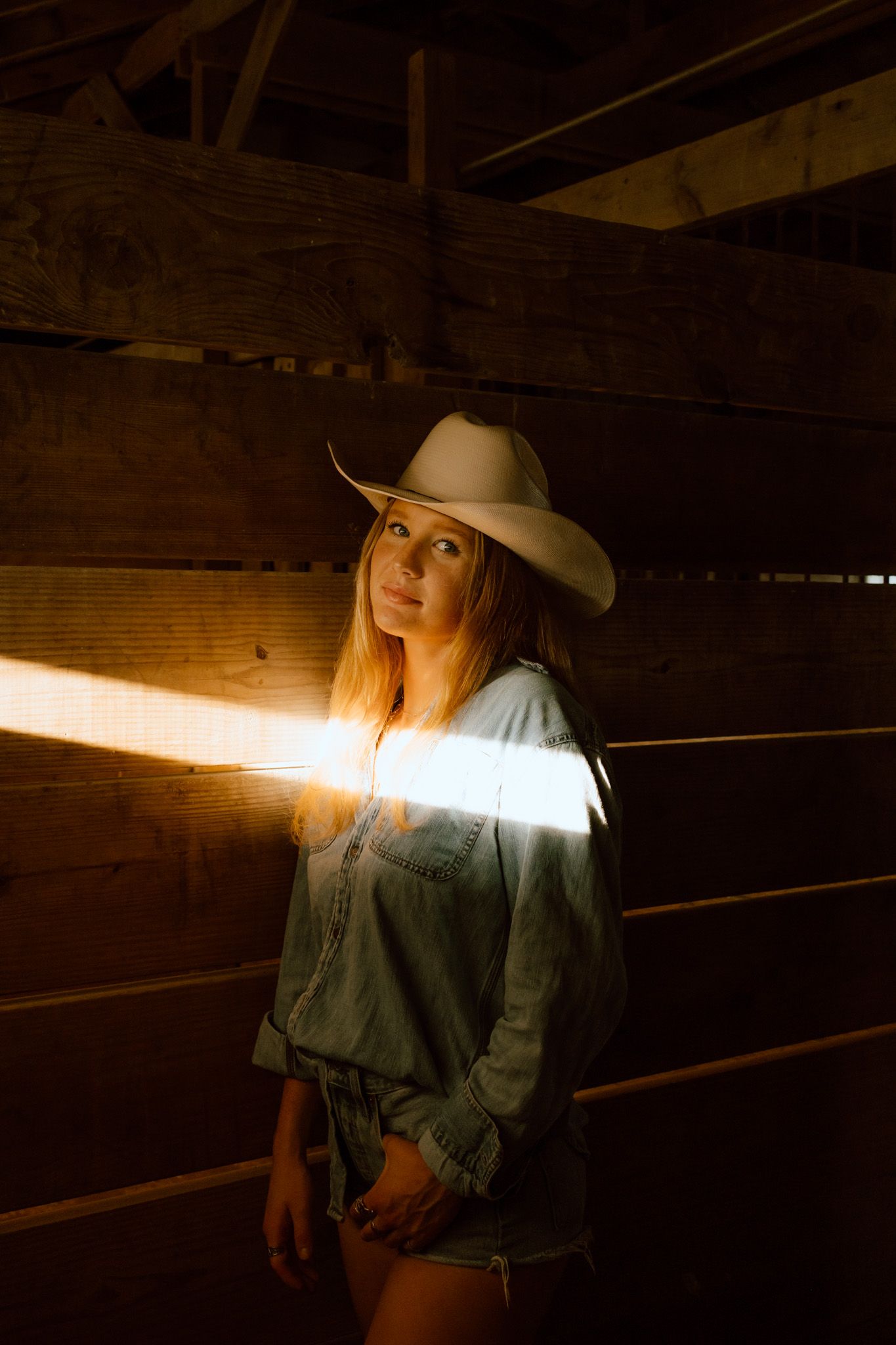 Smiling blonde woman twirling in lace skirt and denim vest on a rural road at dusk.
