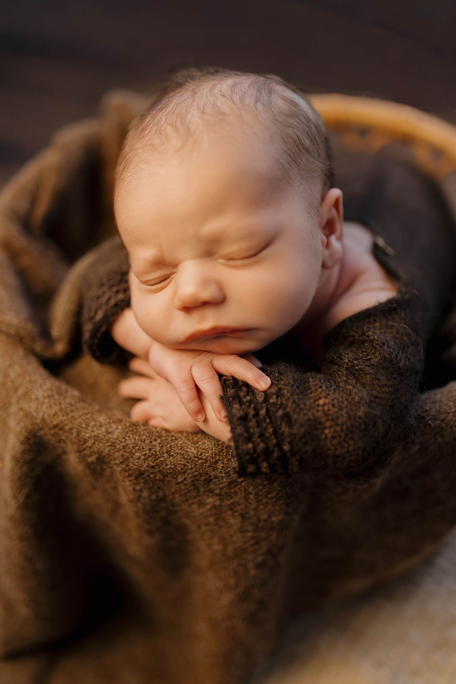 A sleeping newborn wrapped in a soft green knit blanket wears a delicate lace headband on a textured white backdrop.