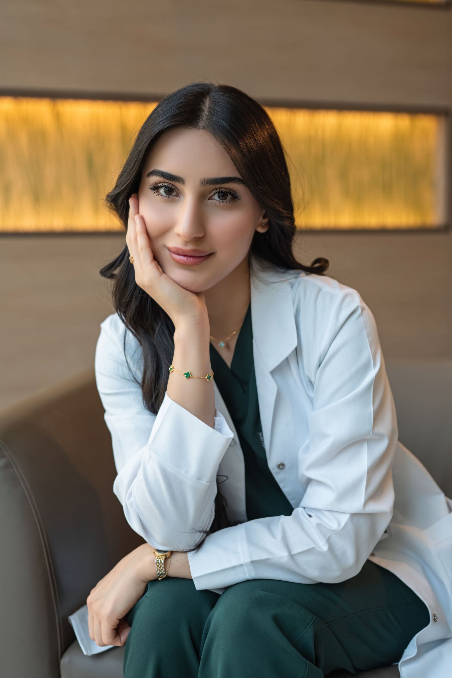 Professional portrait of someone in a white blazer and dark green top resting their chin on their hand.
