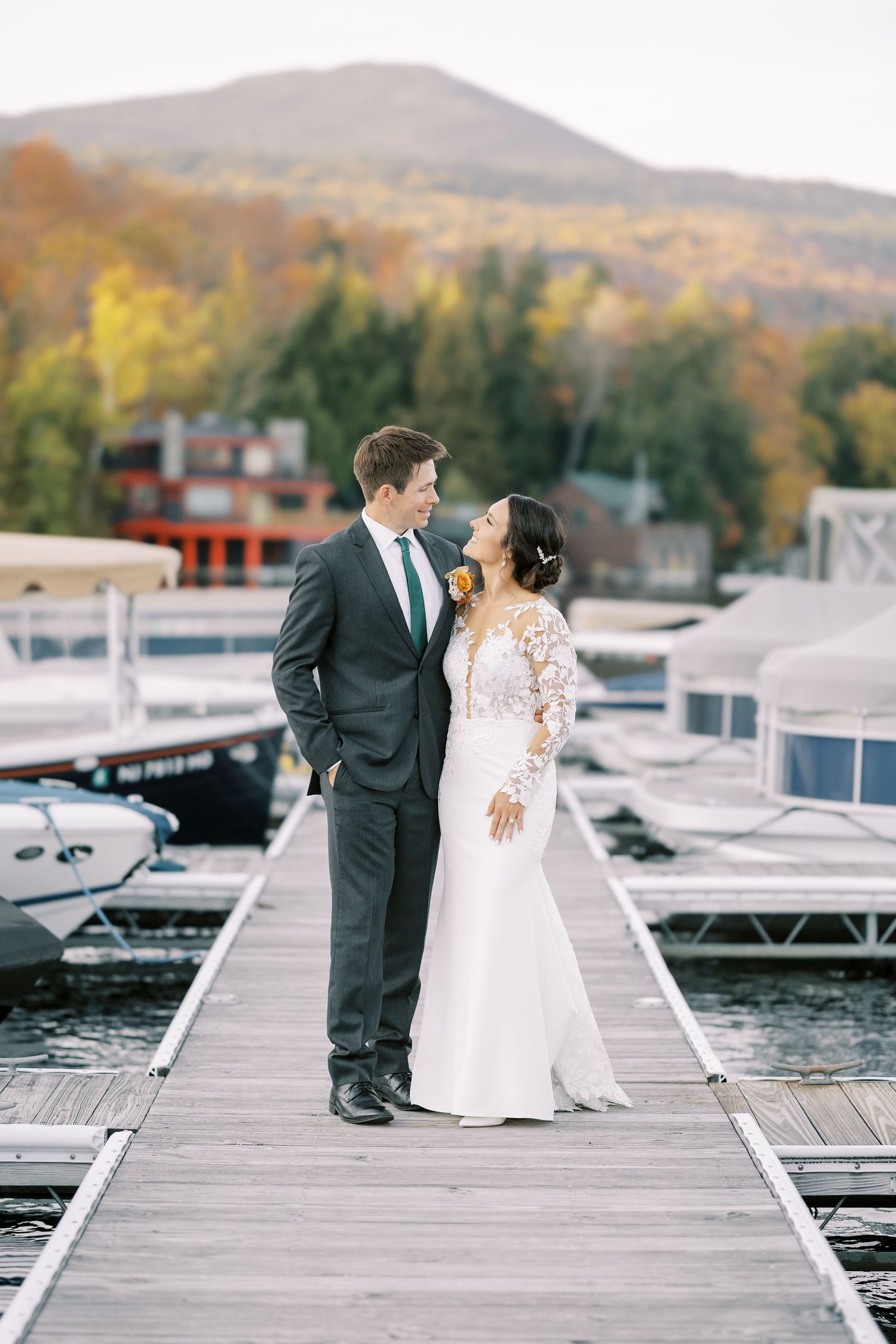 A wedding couple shares romantic moments on a wooden dock by a lake surrounded by autumn foliage in the mountains.