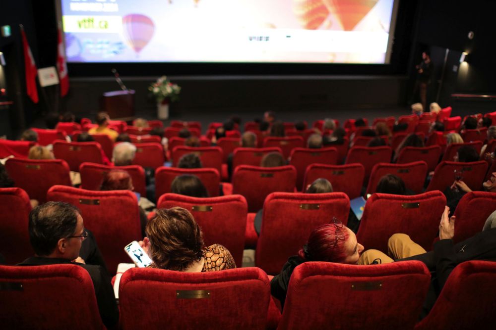 Movie theater audience watching a film from behind in red seats with a bright screen in the background.